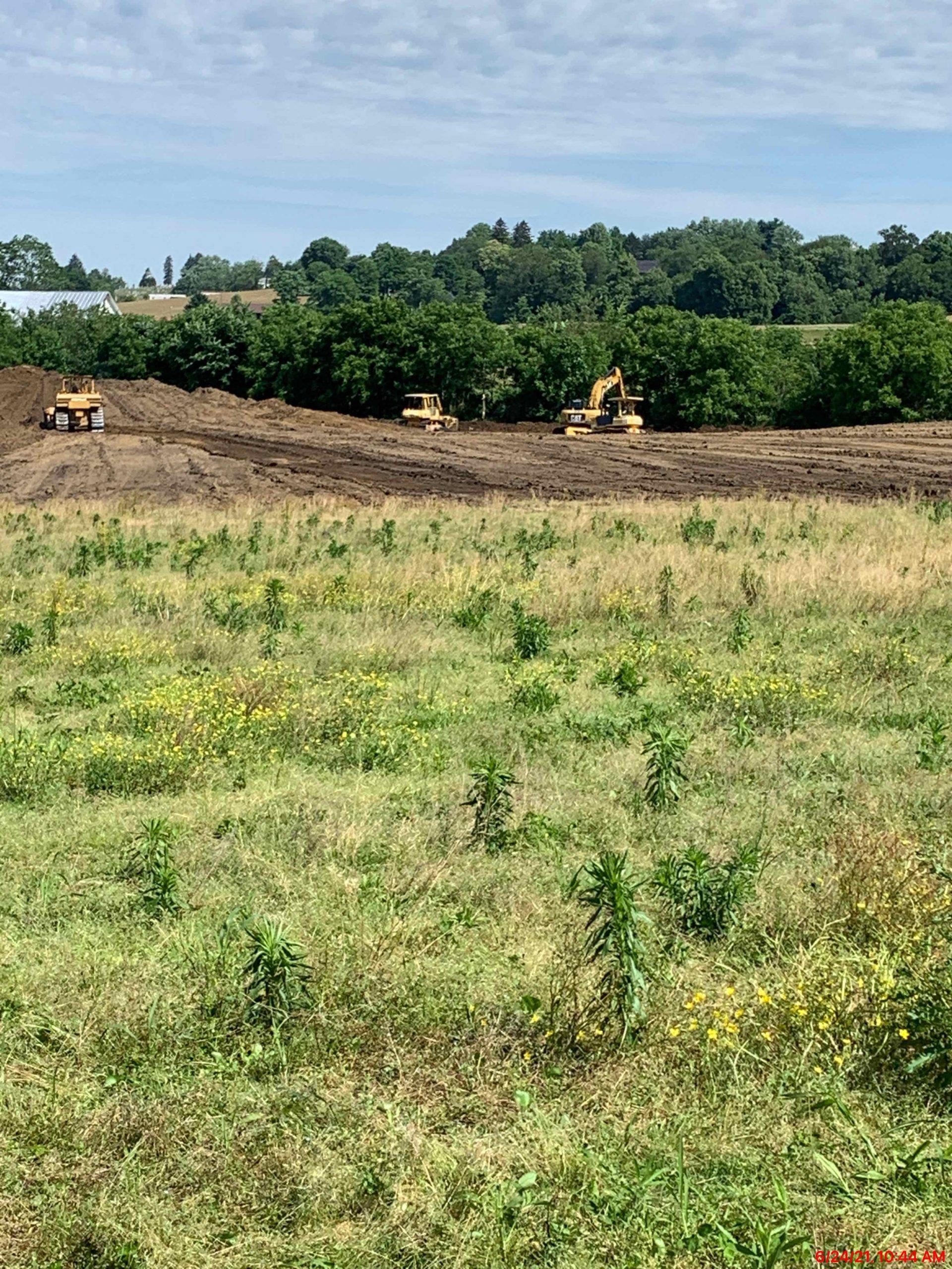 Construction site with three heavy machines working on a brown field. Green field in the foreground.