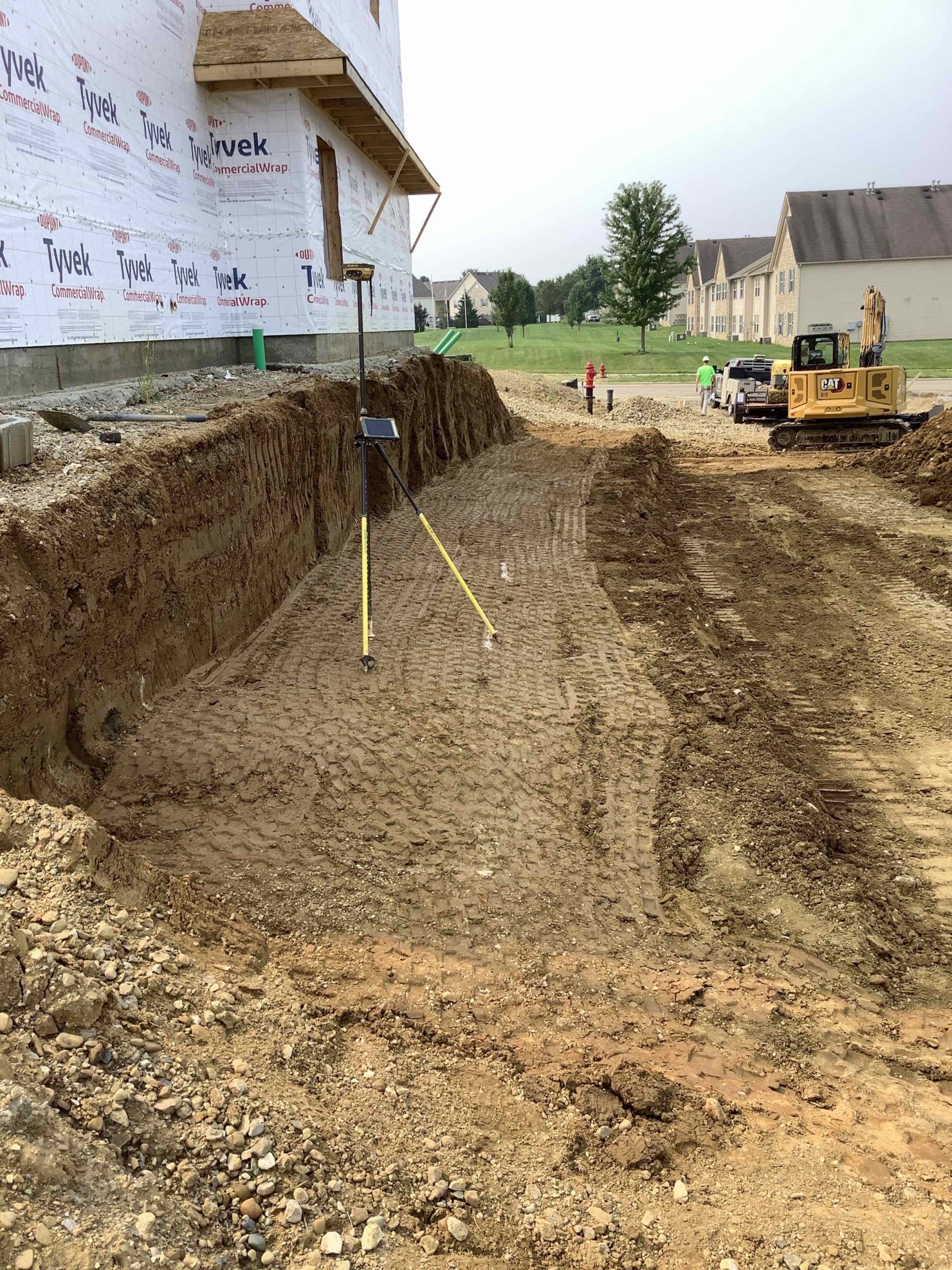 Construction site with excavated earth, partially built house, and a small excavator.