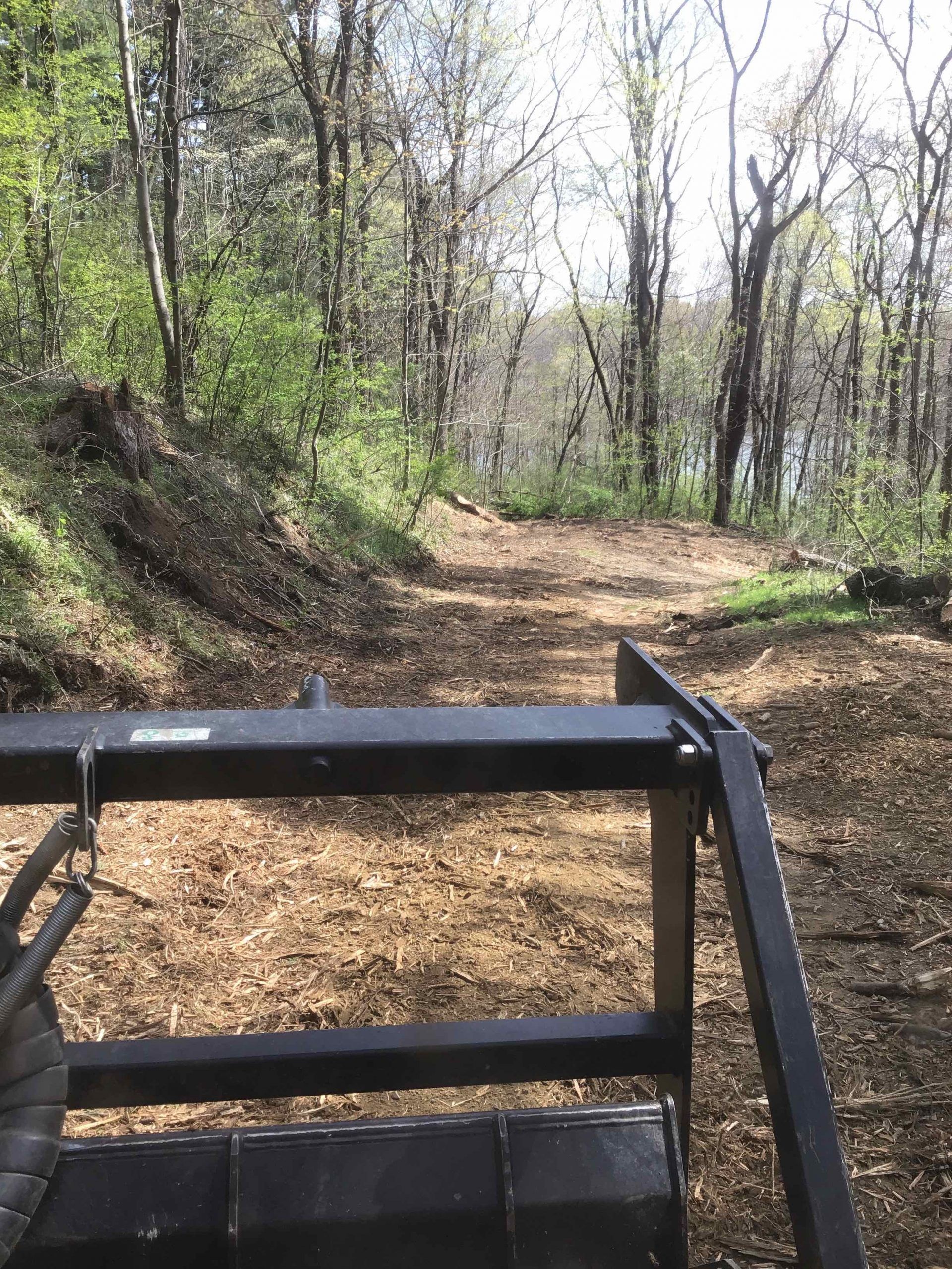 A view from a tractor looking up a dirt path in a wooded area. Wood chips cover the path.