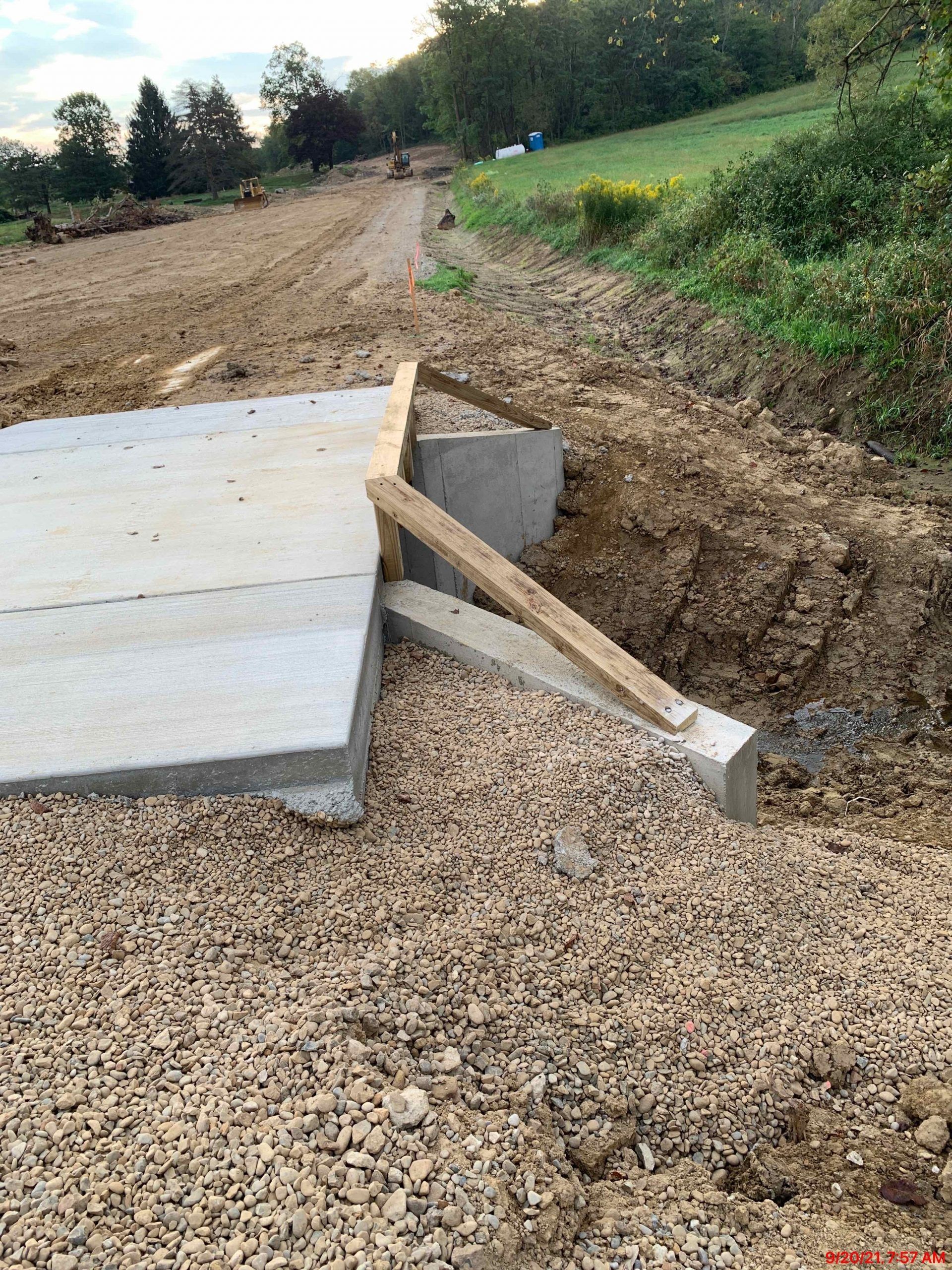 Concrete slab partially constructed on a gravel base next to a dirt path. Wooden supports are visible.