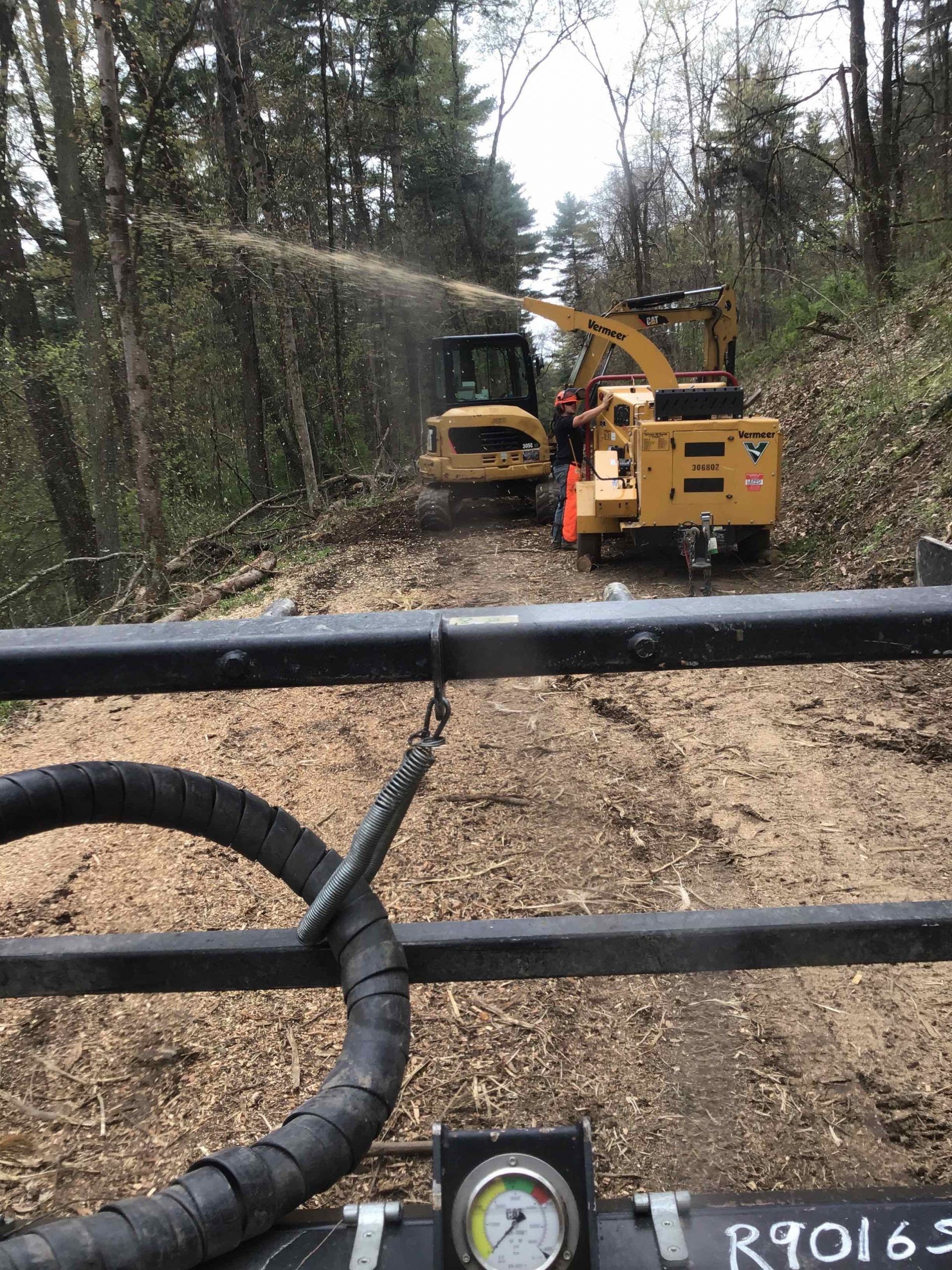 Wood chipper and excavator clearing a wooded area. Chips flying.
