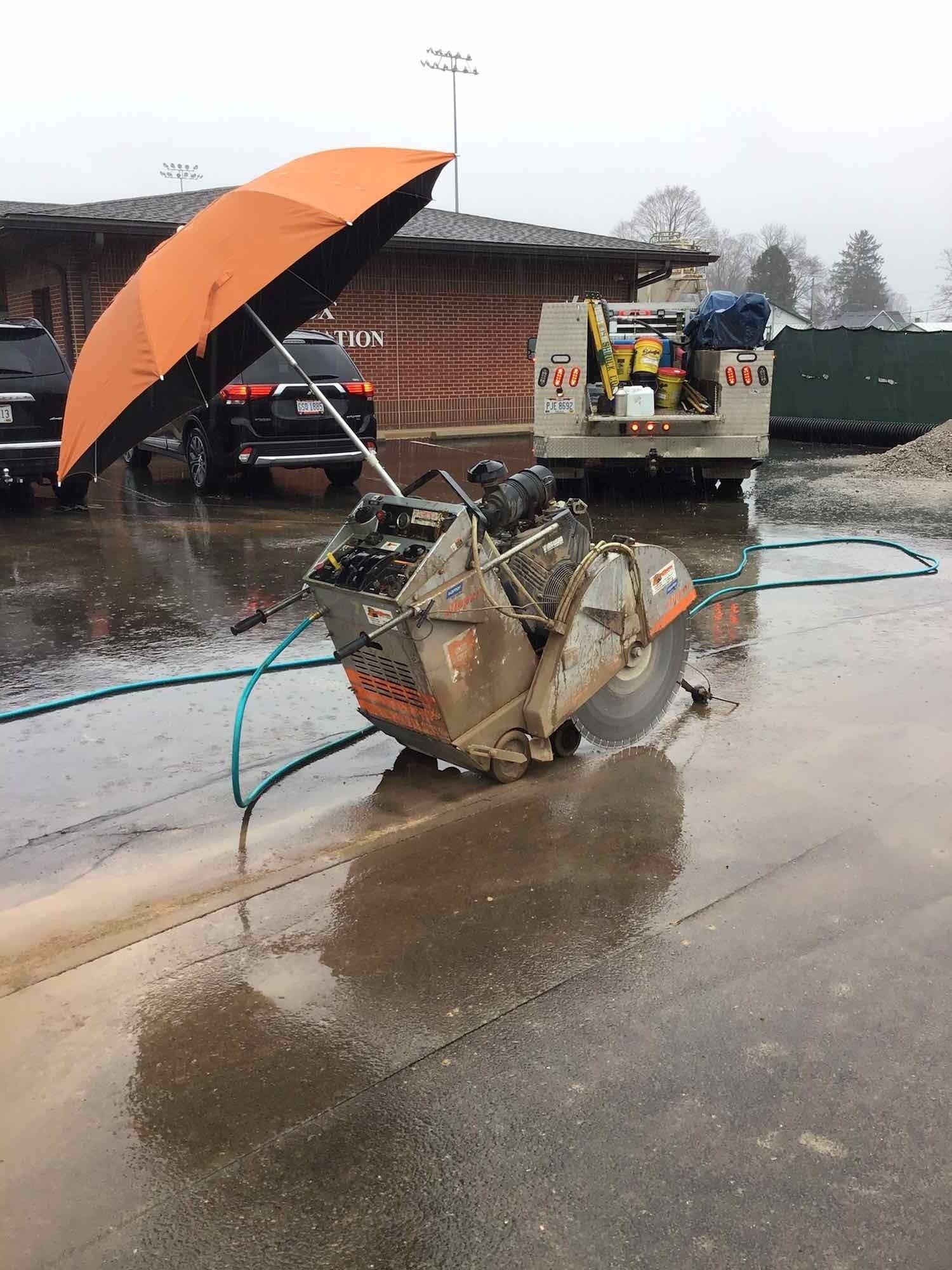Concrete saw with orange umbrella in the rain.