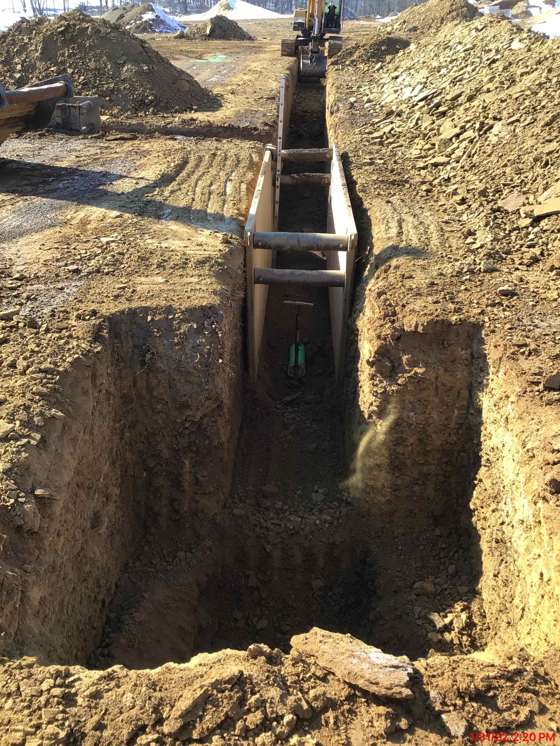 Trench being dug with shoring to prevent collapse, likely for underground utility work on a construction site.
