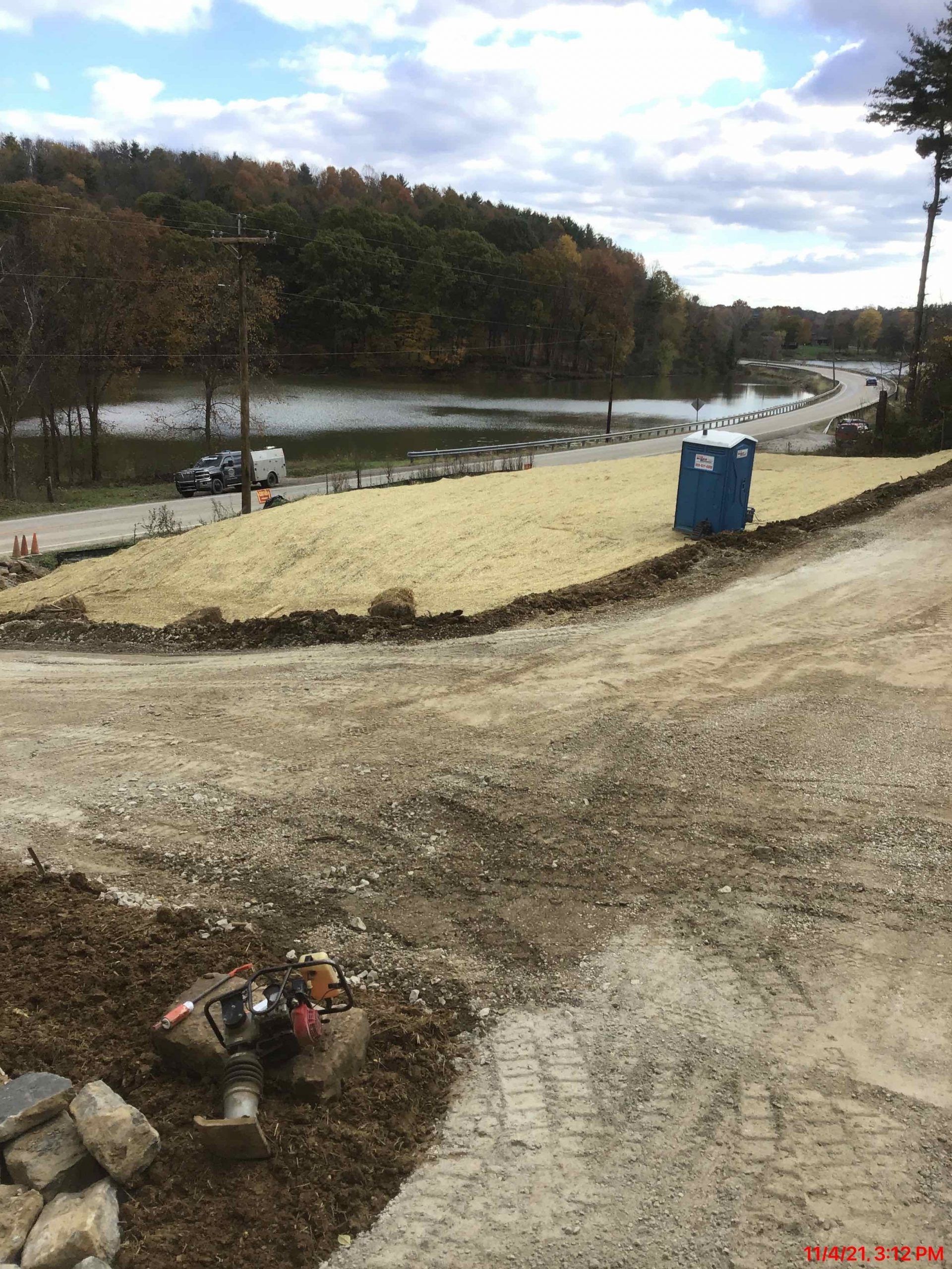 Construction site with dirt, gravel, and a blue portable toilet next to a river.