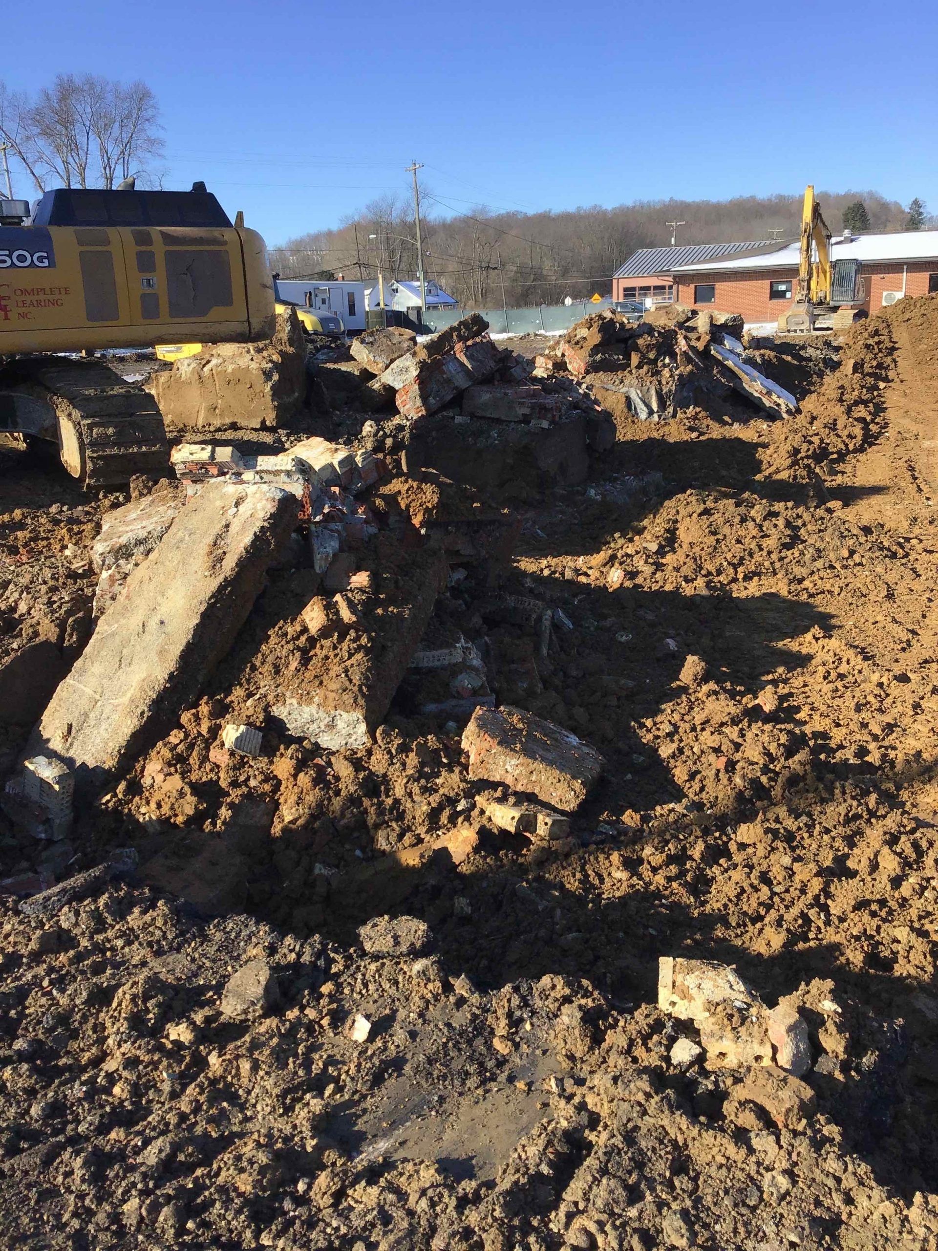 Construction site: excavator and rubble pile, dirt ground, clear sky.