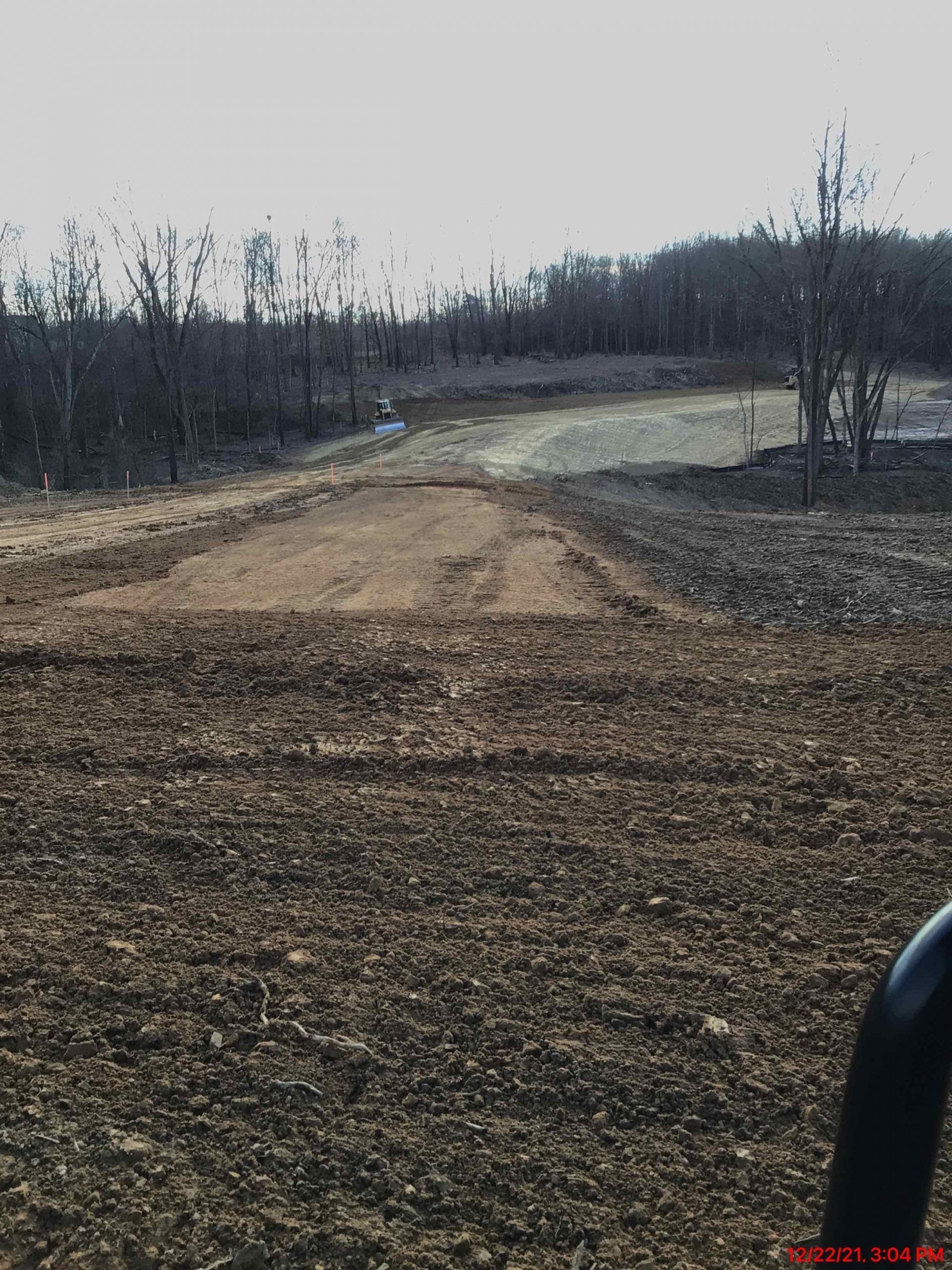 Dirt road under construction, surrounded by bare trees, sunny day.