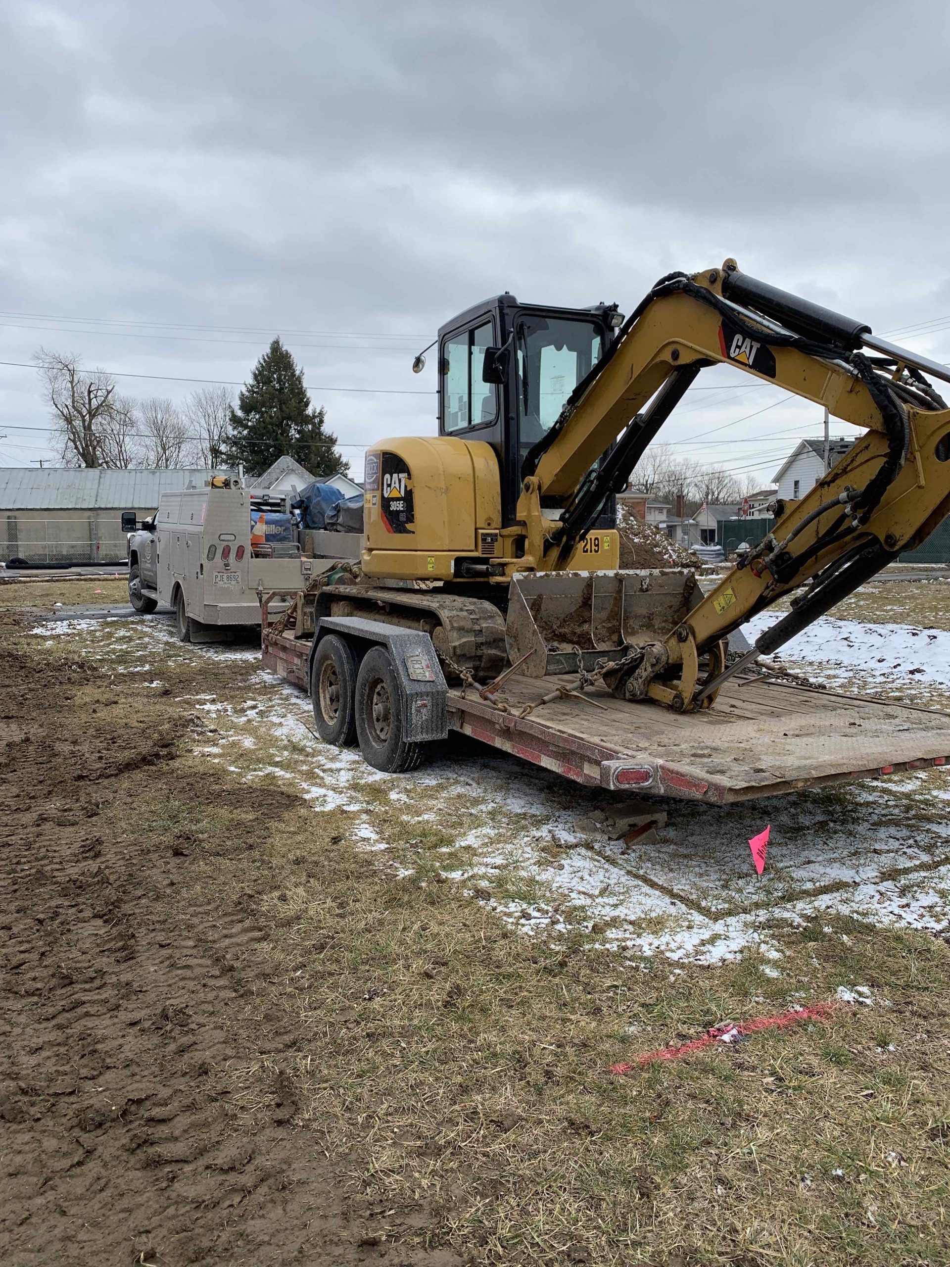 Yellow excavator on a trailer parked in a muddy field on an overcast day.