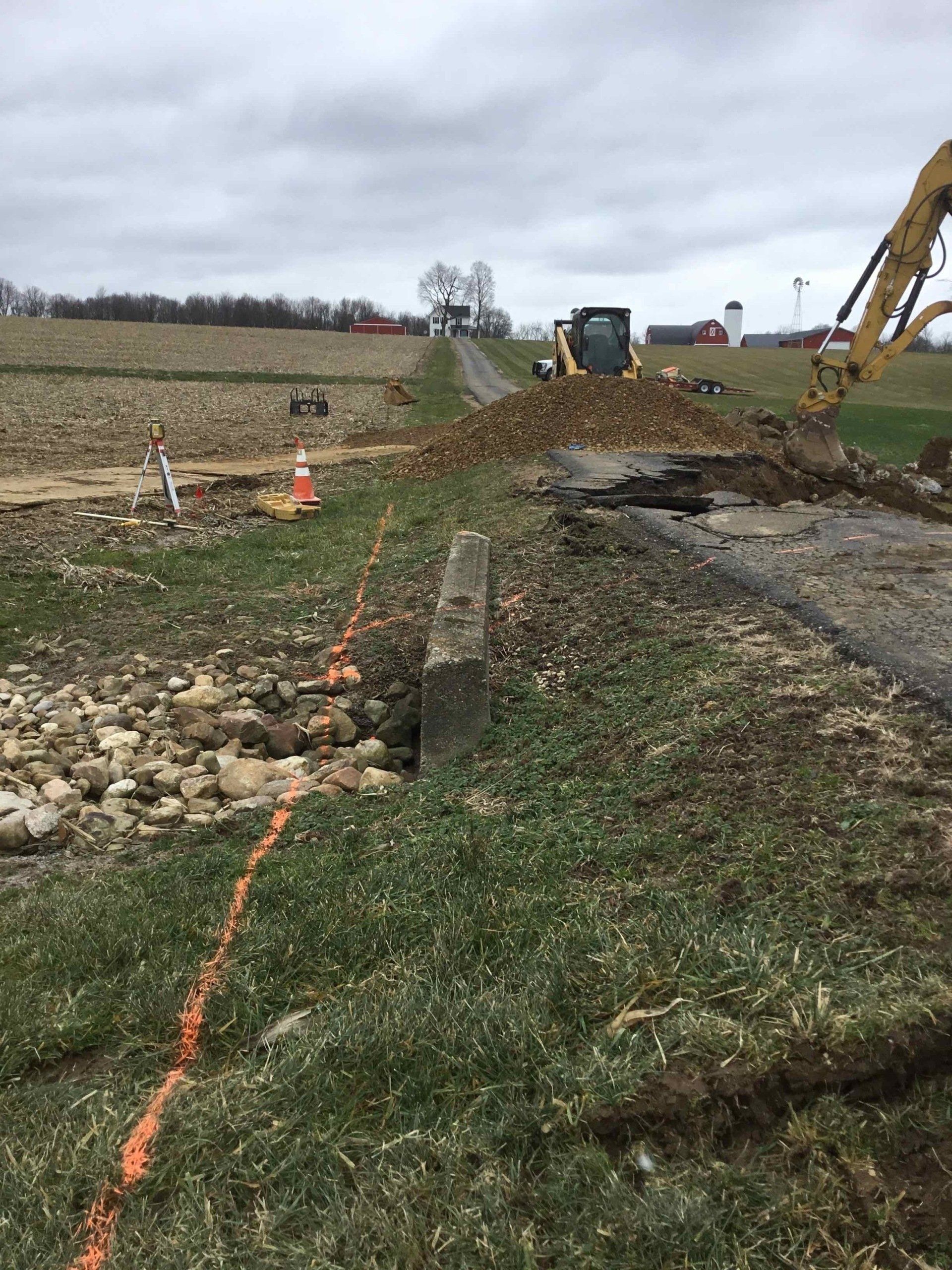 Construction site with excavator and road work near a field.