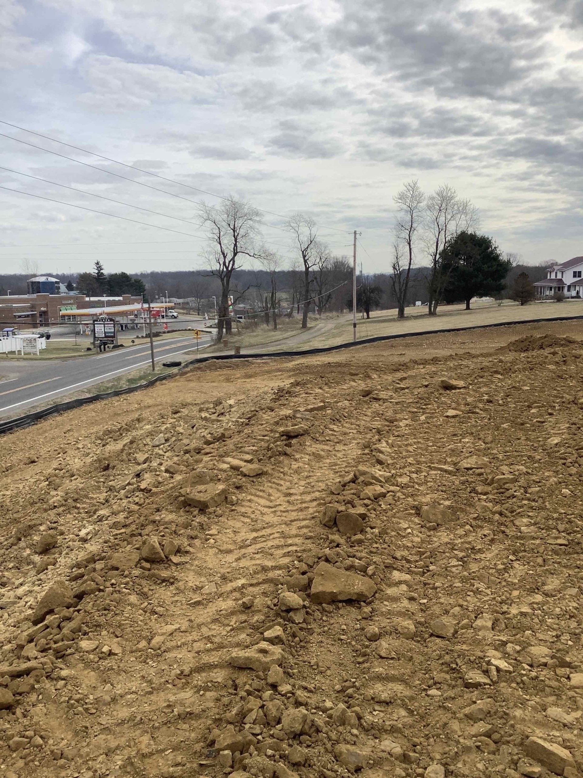 A dirt hillside overlooks a road with buildings and cloudy sky in the background.