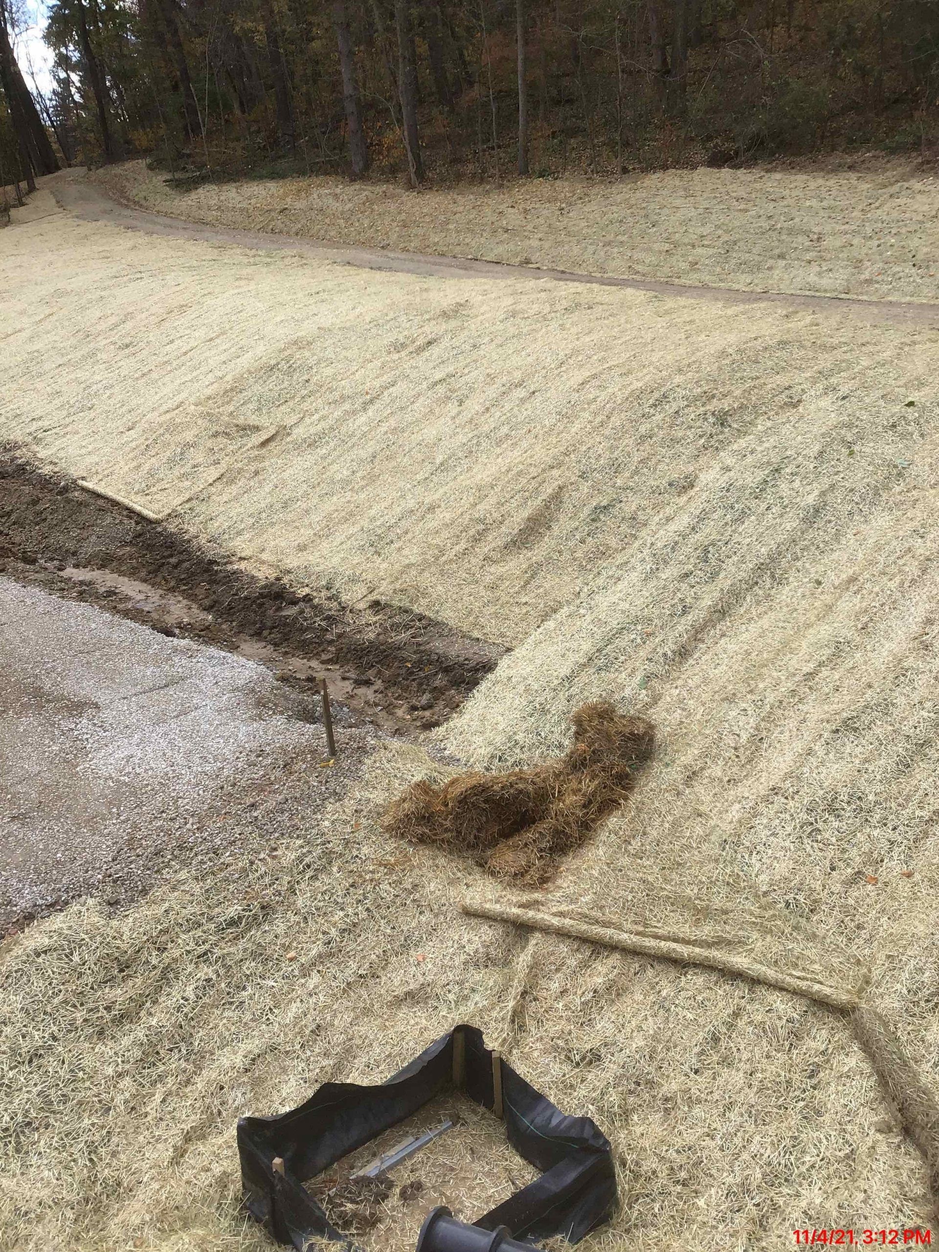 Sloped area covered in light-colored mulch, with a black rectangular structure at the bottom.