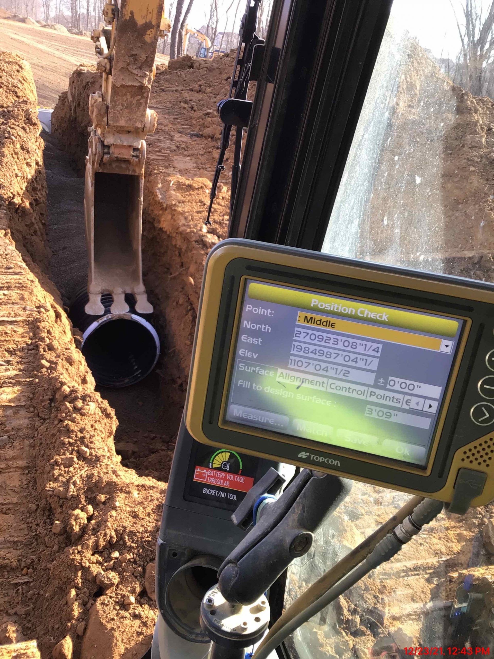 Excavator digging a trench, with screen displaying data, for laying pipes.