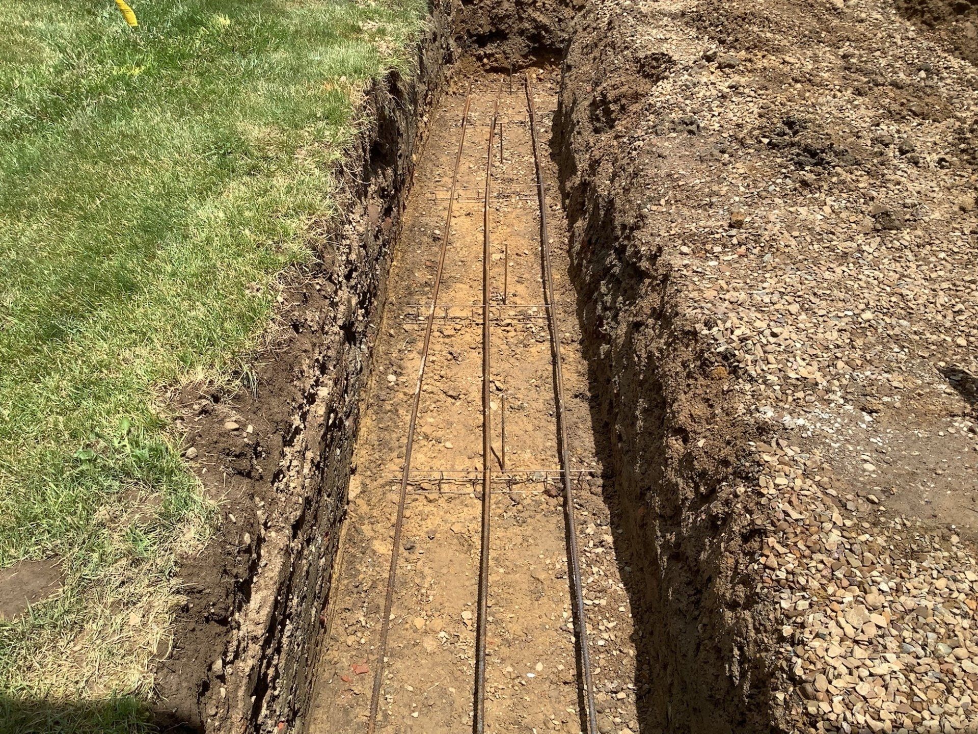 A trench in the ground with rebar laid, likely for a concrete foundation, next to grass.