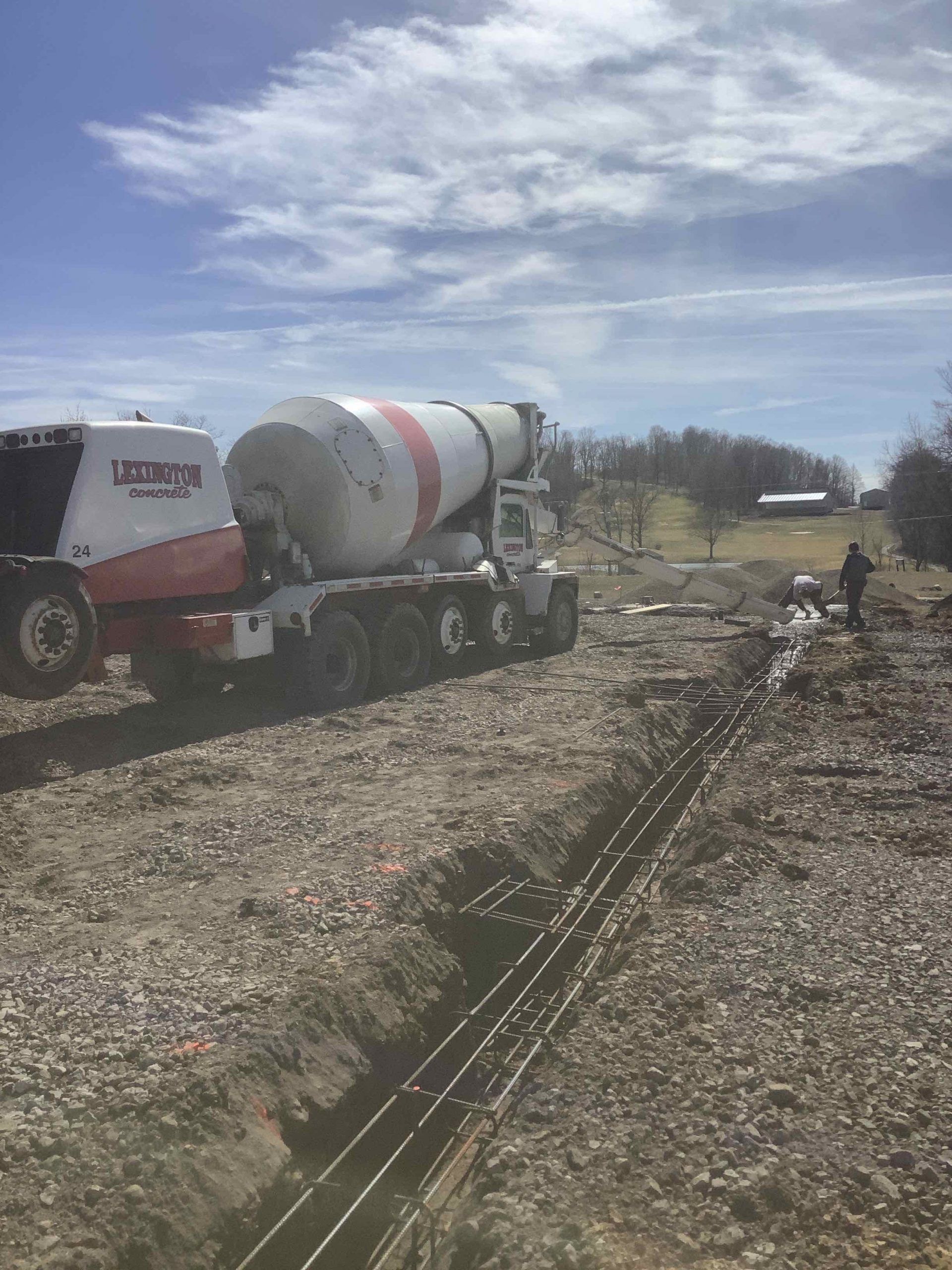 Cement truck pouring concrete into a prepared trench on a construction site; sunny day.