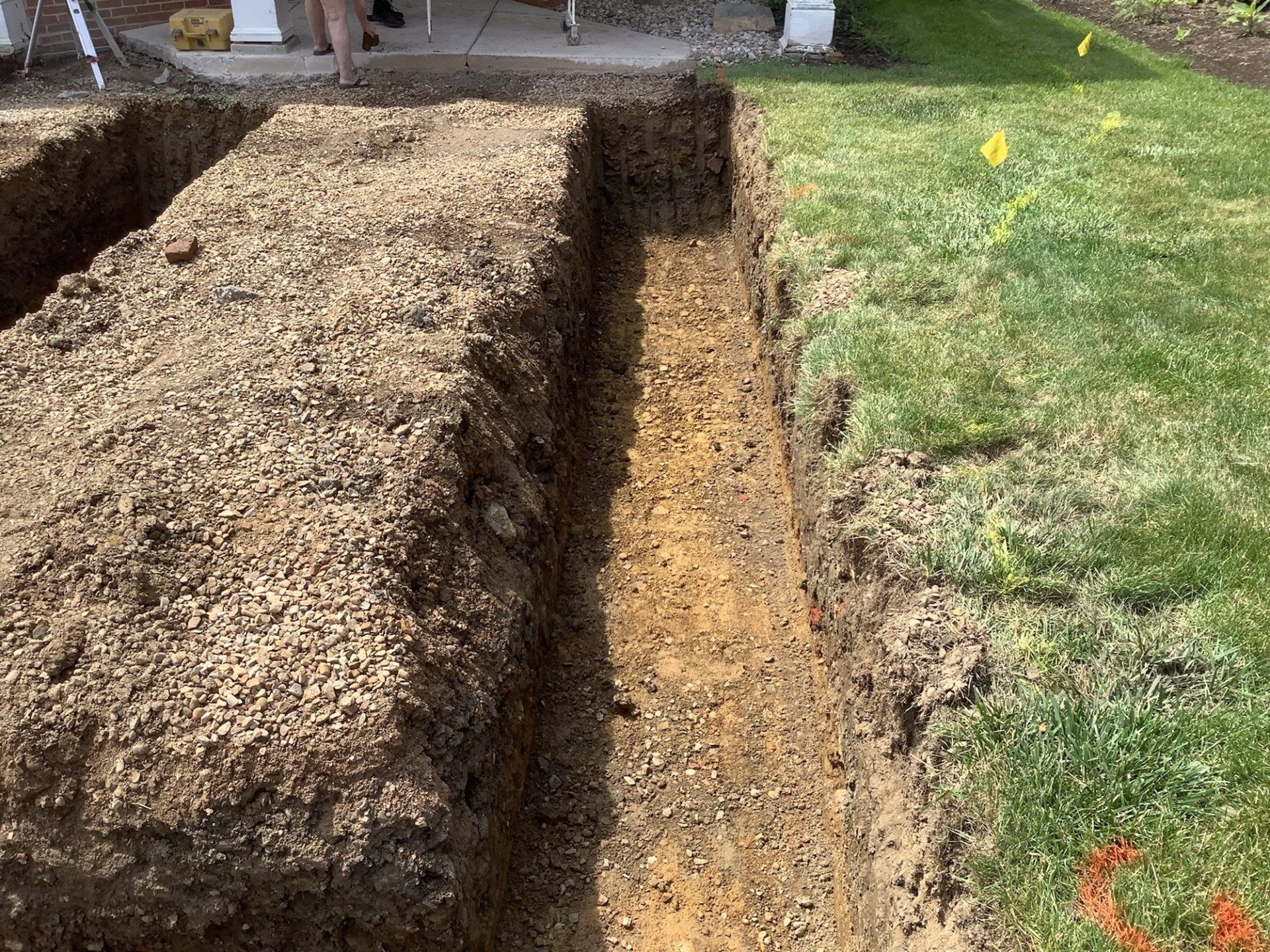 Trenches dug in ground, next to green grass and a patio.