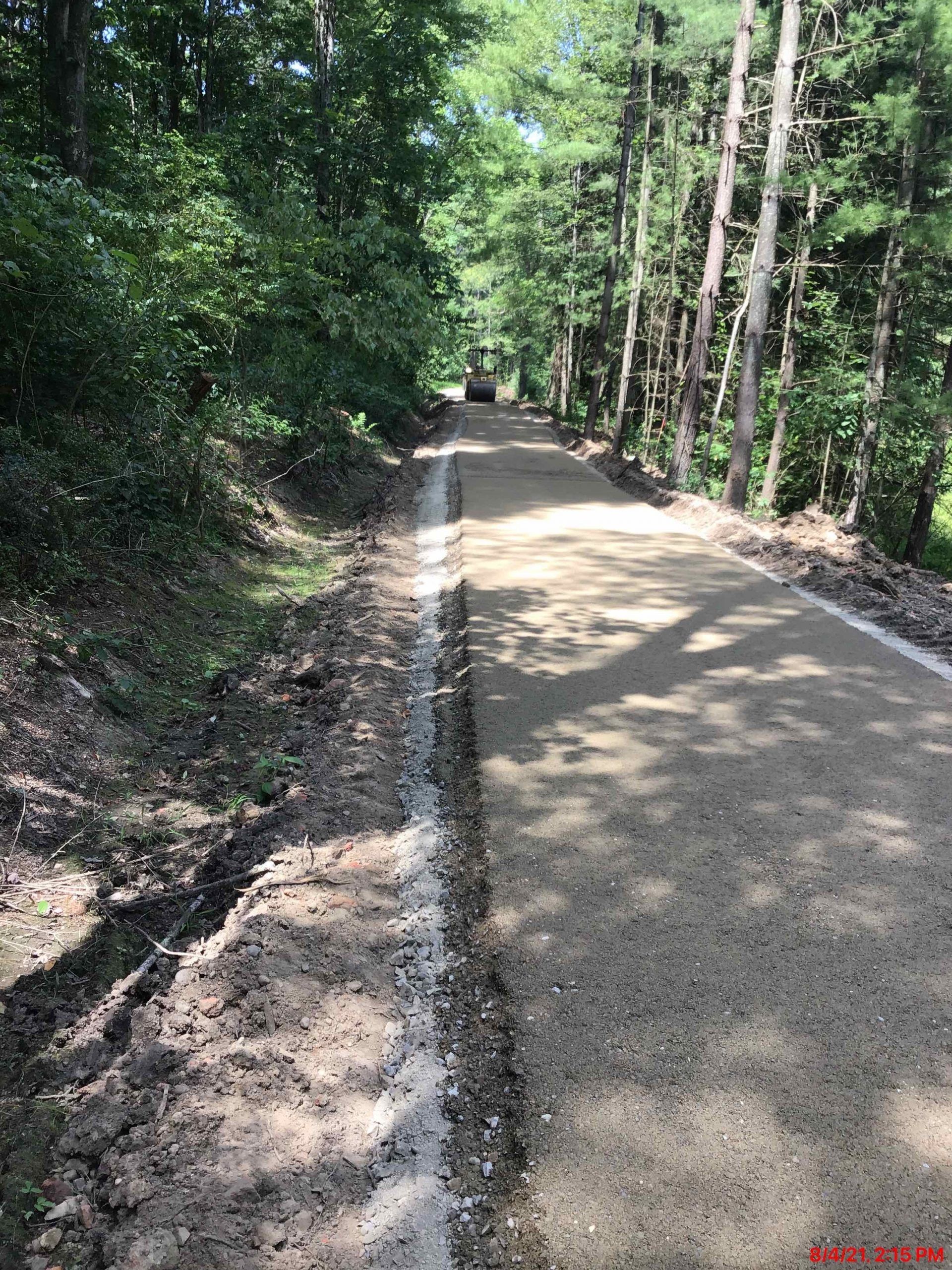 Gravel road through a forest with muddy edge. Trees line both sides. Heavy machinery is at the end.