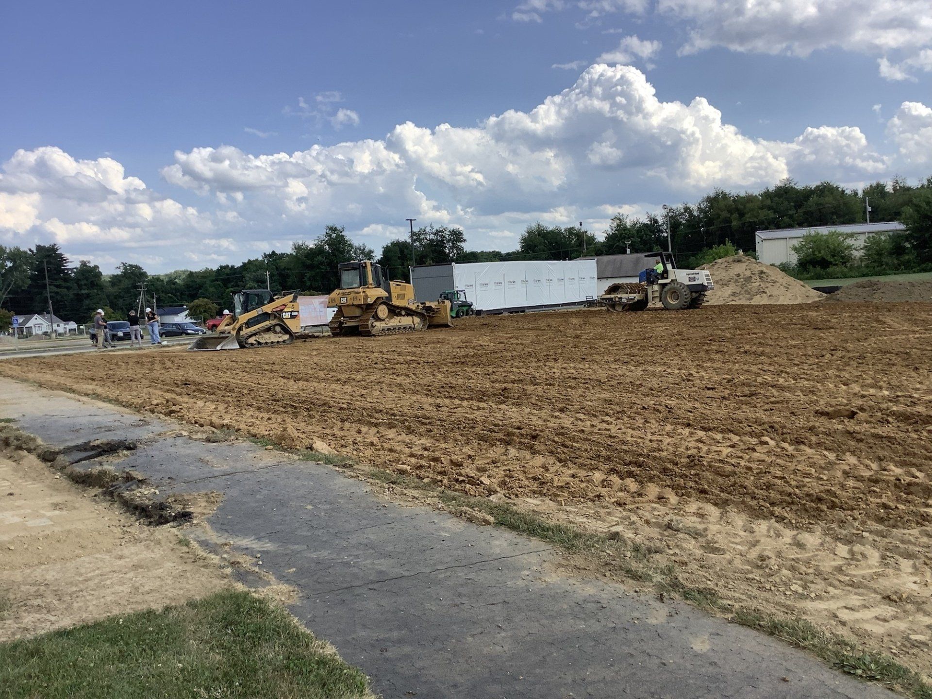 Construction site with bulldozers and equipment grading a large area of dirt under a cloudy sky.