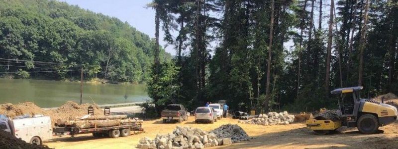 Construction site by a lake with trees and heavy machinery.