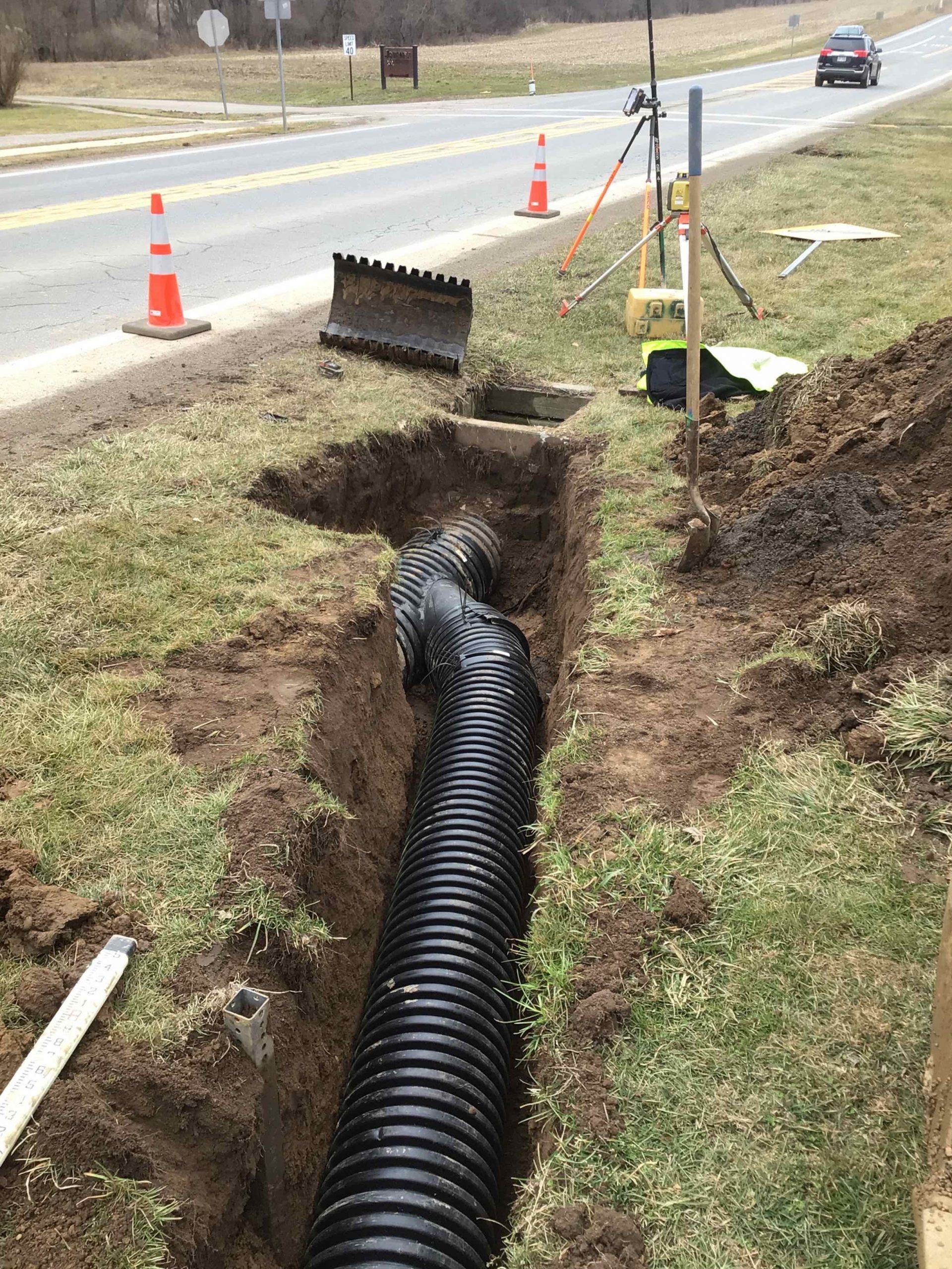 A trench with a black corrugated pipe running through it, beside a road.