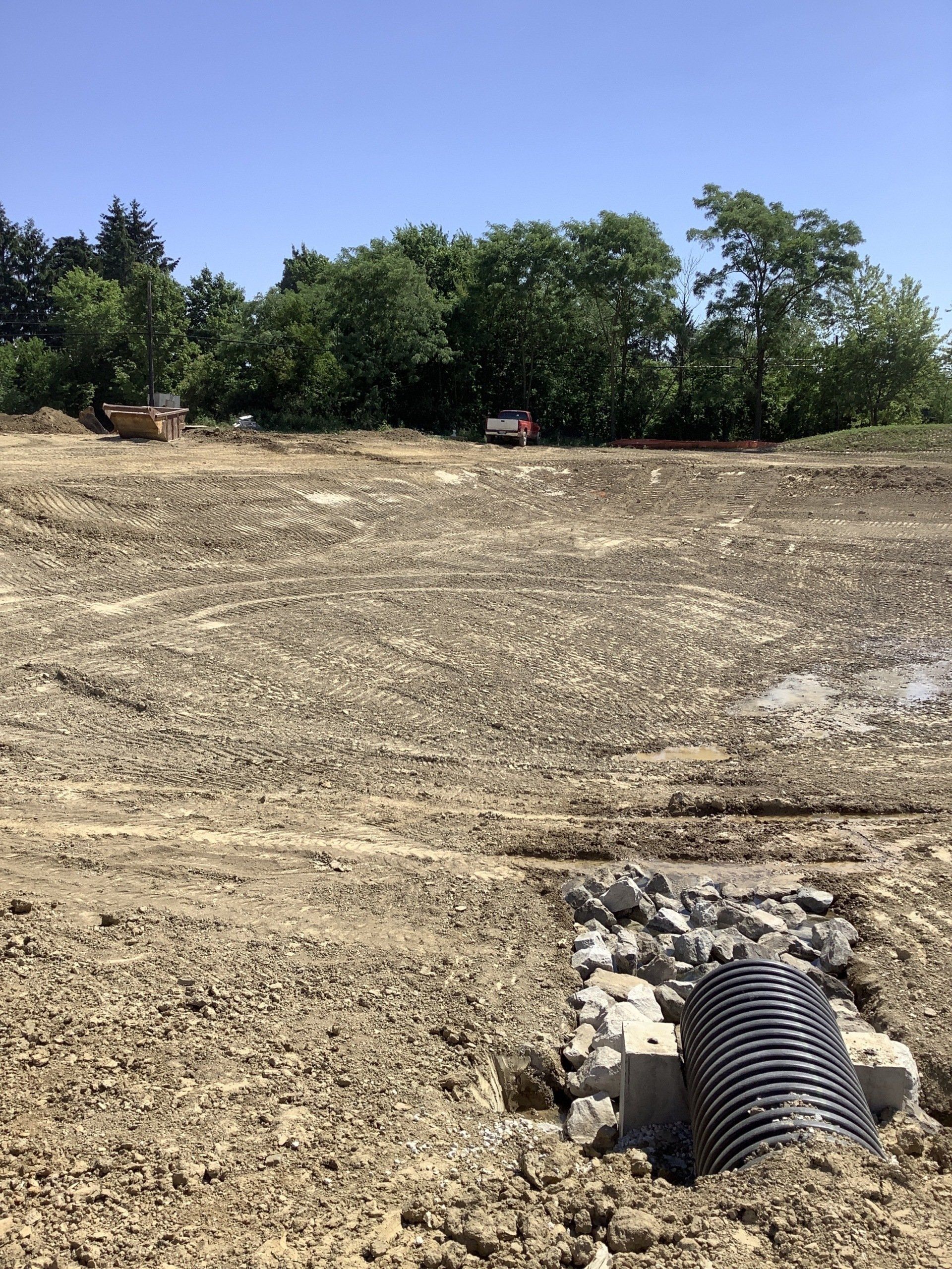 Construction site, muddy ground, black pipe, rocks, trees, blue sky.
