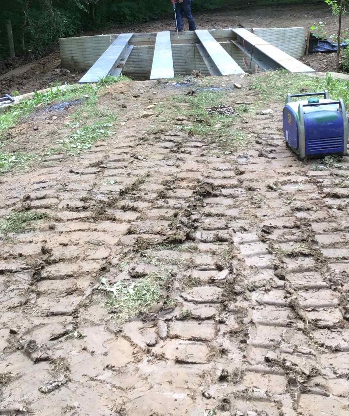 Muddy dirt road with tractor tire tracks leading to a concrete structure; a person is standing on the structure.