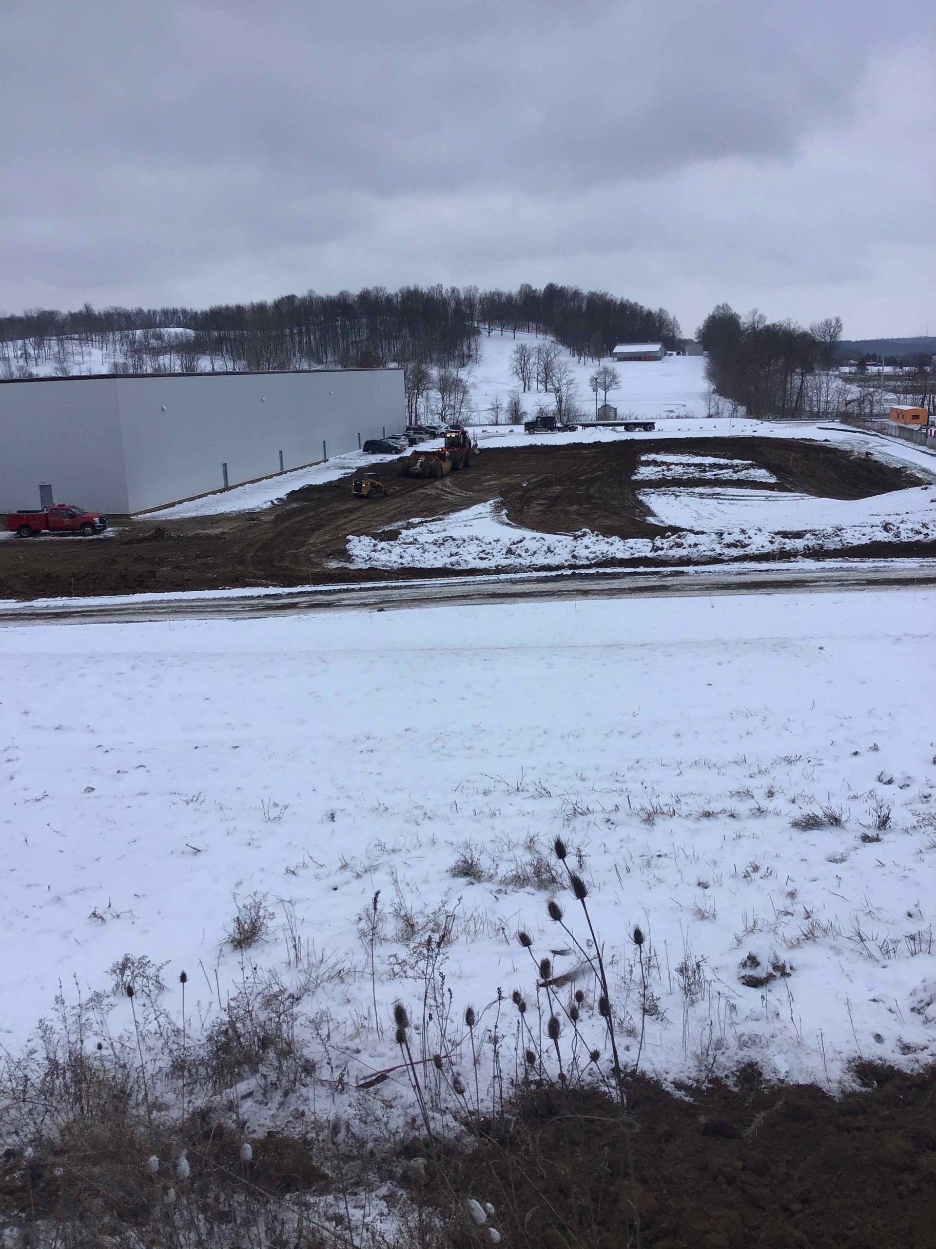 Snowy landscape with construction site in the background and a large white building to the left.