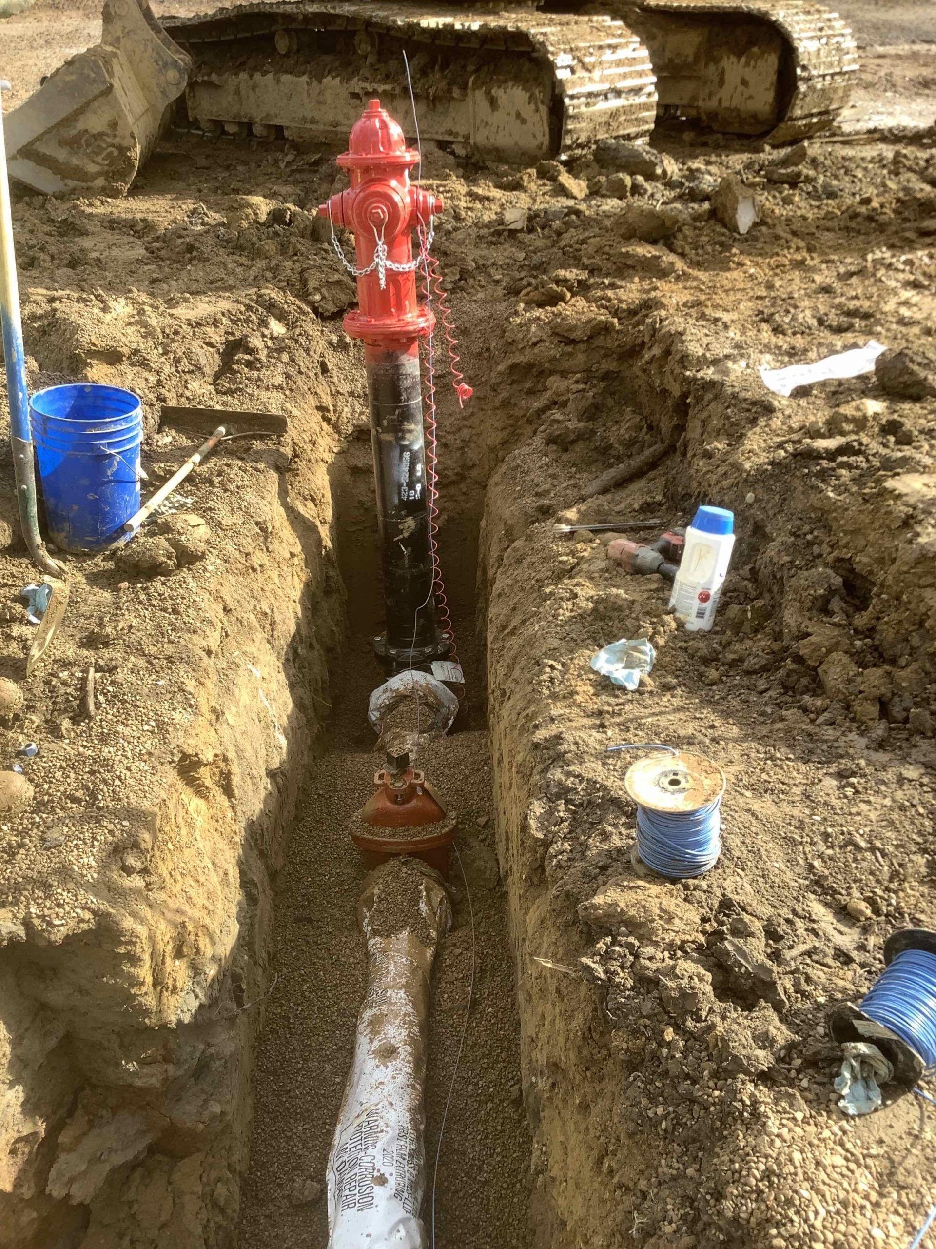 A red fire hydrant installed in a trench with exposed pipes and construction materials.