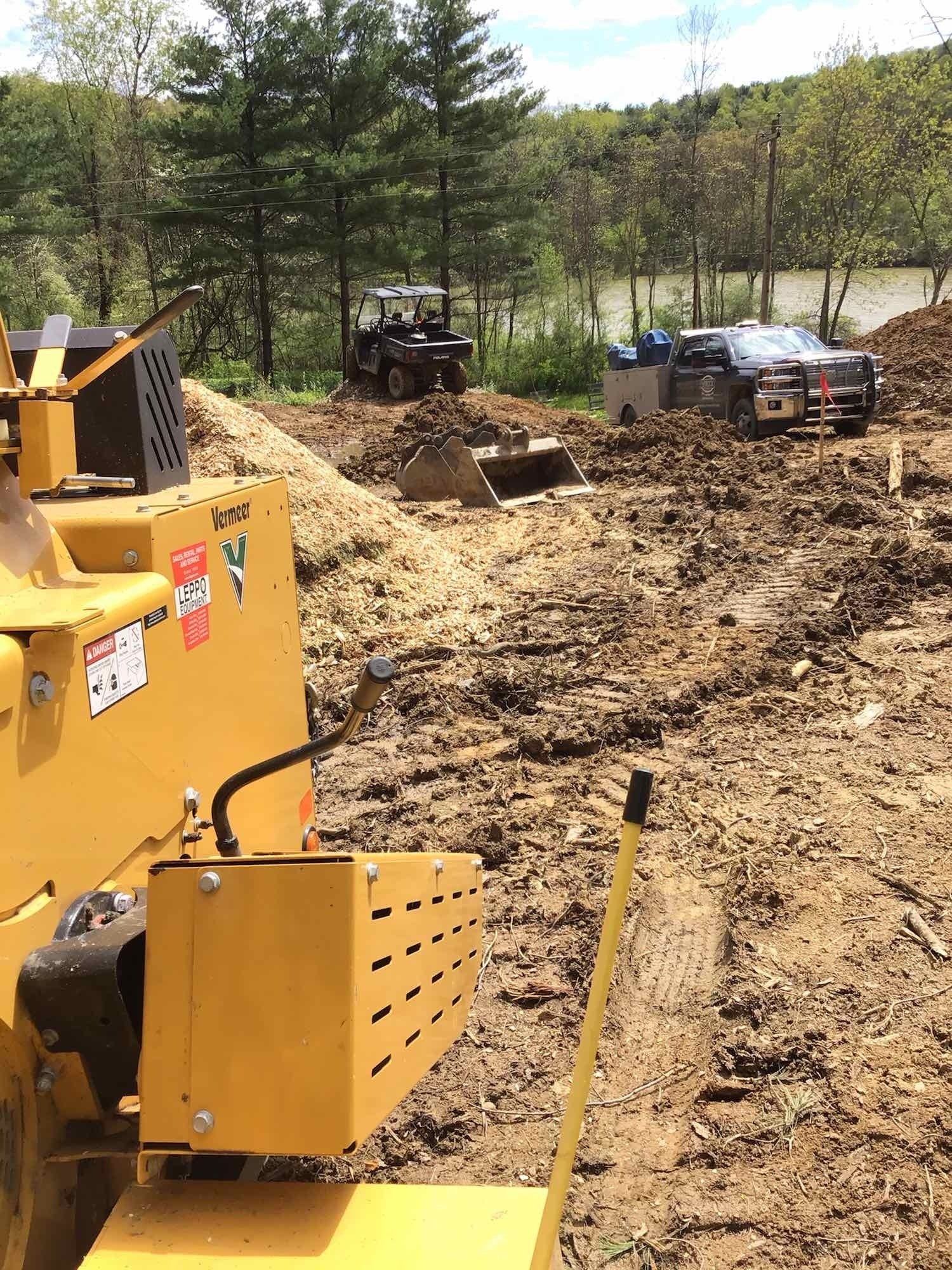 Yellow wood chipper and police vehicles in a muddy clearing.