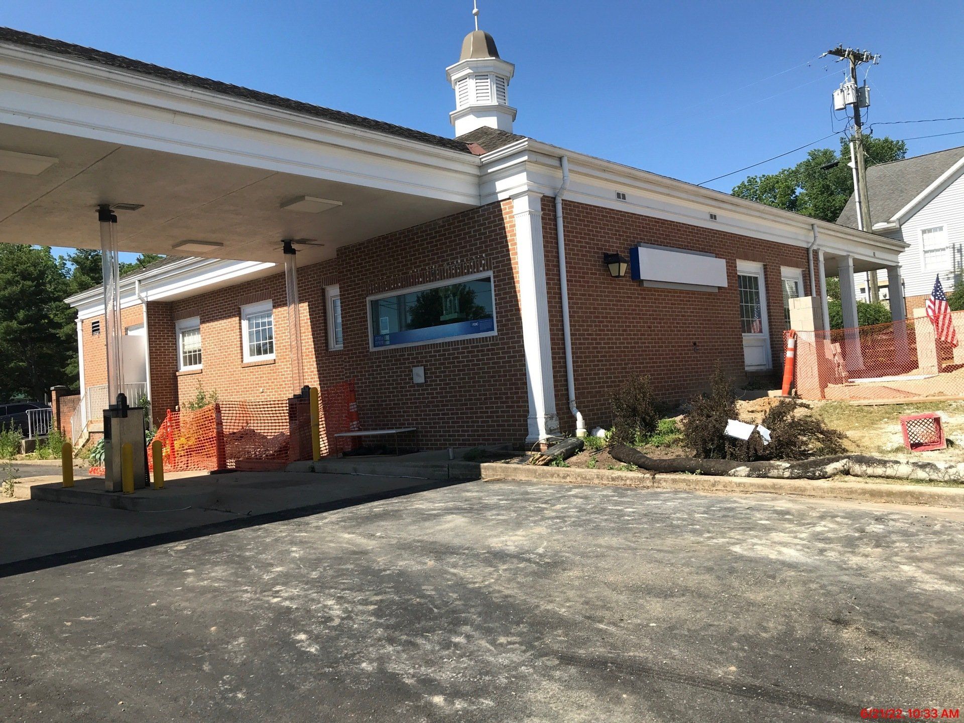 Brick building, possibly a former bank, under construction with orange barriers and a drive-thru canopy.