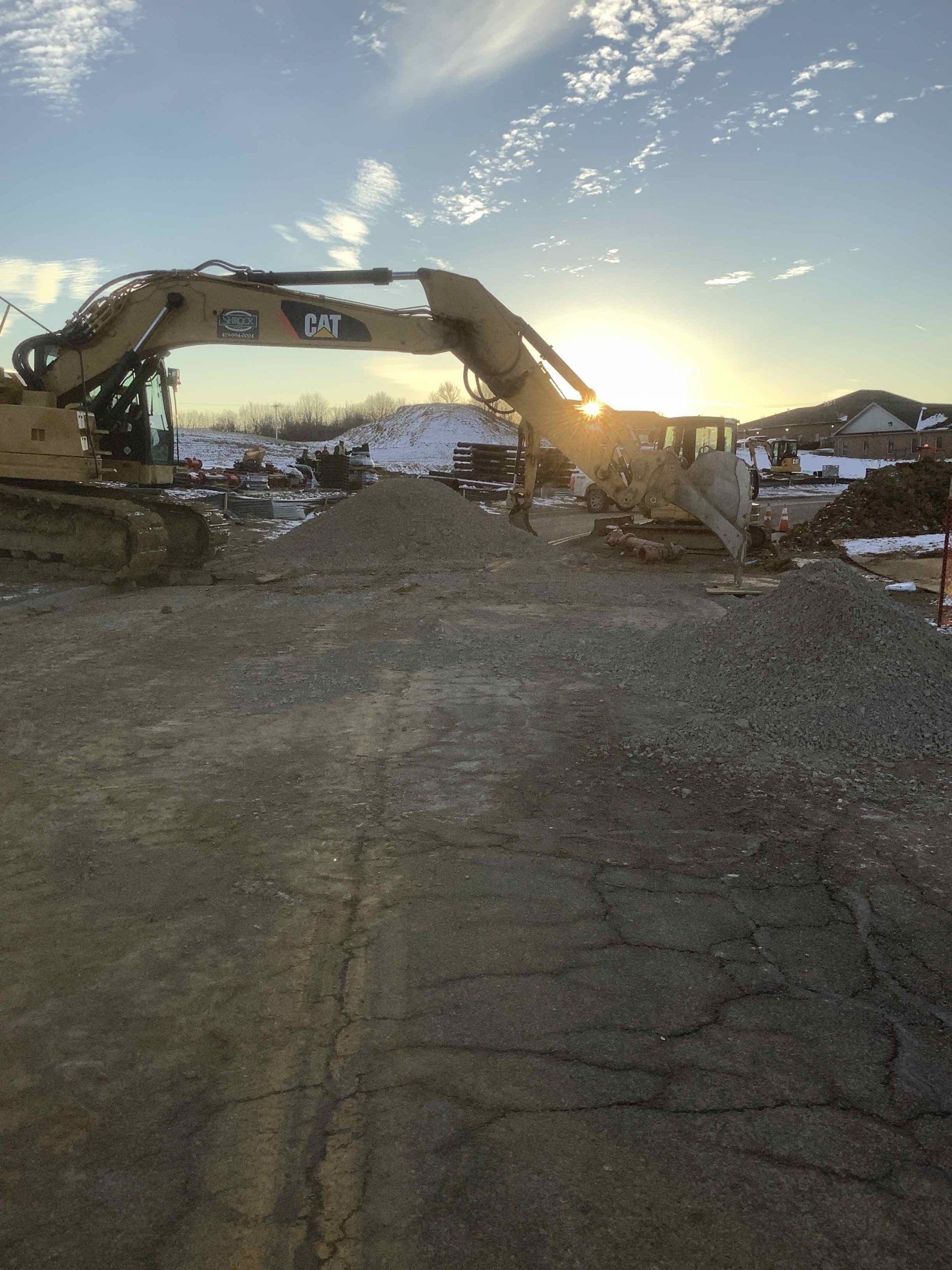Excavator at work on a construction site; the sun sets in the background.