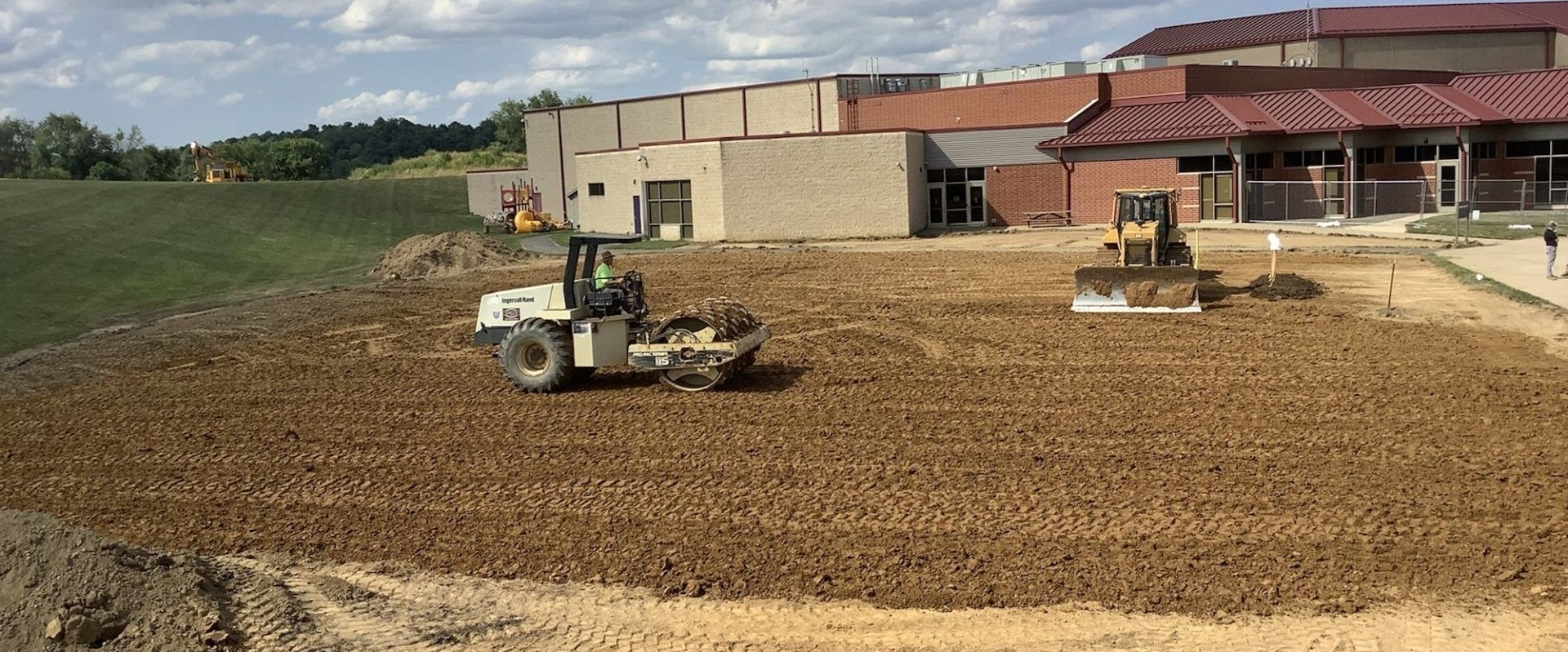 Construction site with two pieces of heavy machinery working on the ground. A building is in the background.