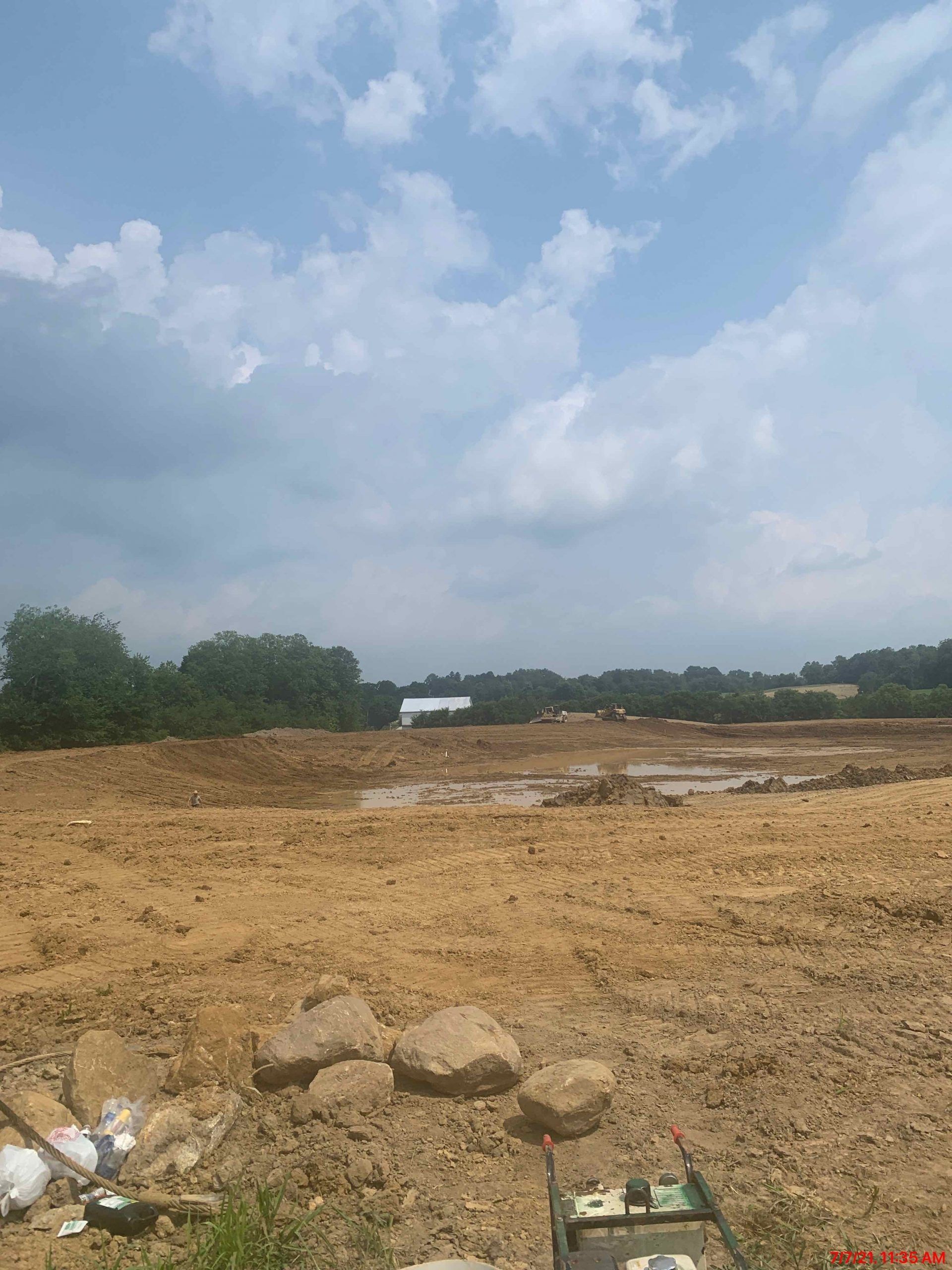 Brown dirt field under a cloudy blue sky. Trees in the distance.