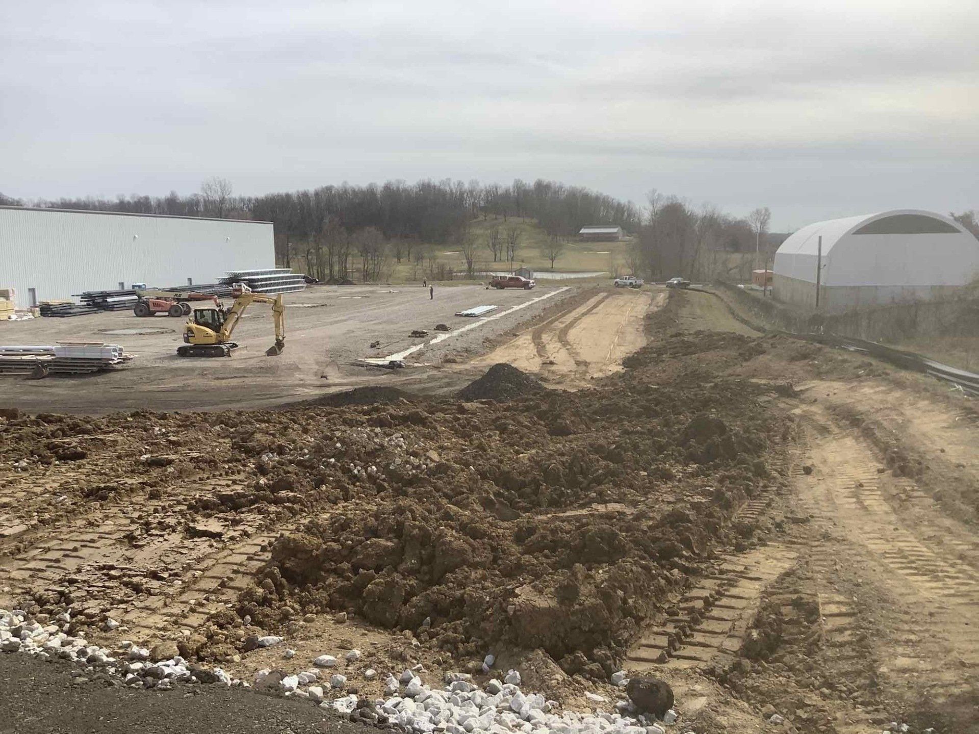 Construction site: dirt piles, equipment, and buildings under overcast sky.