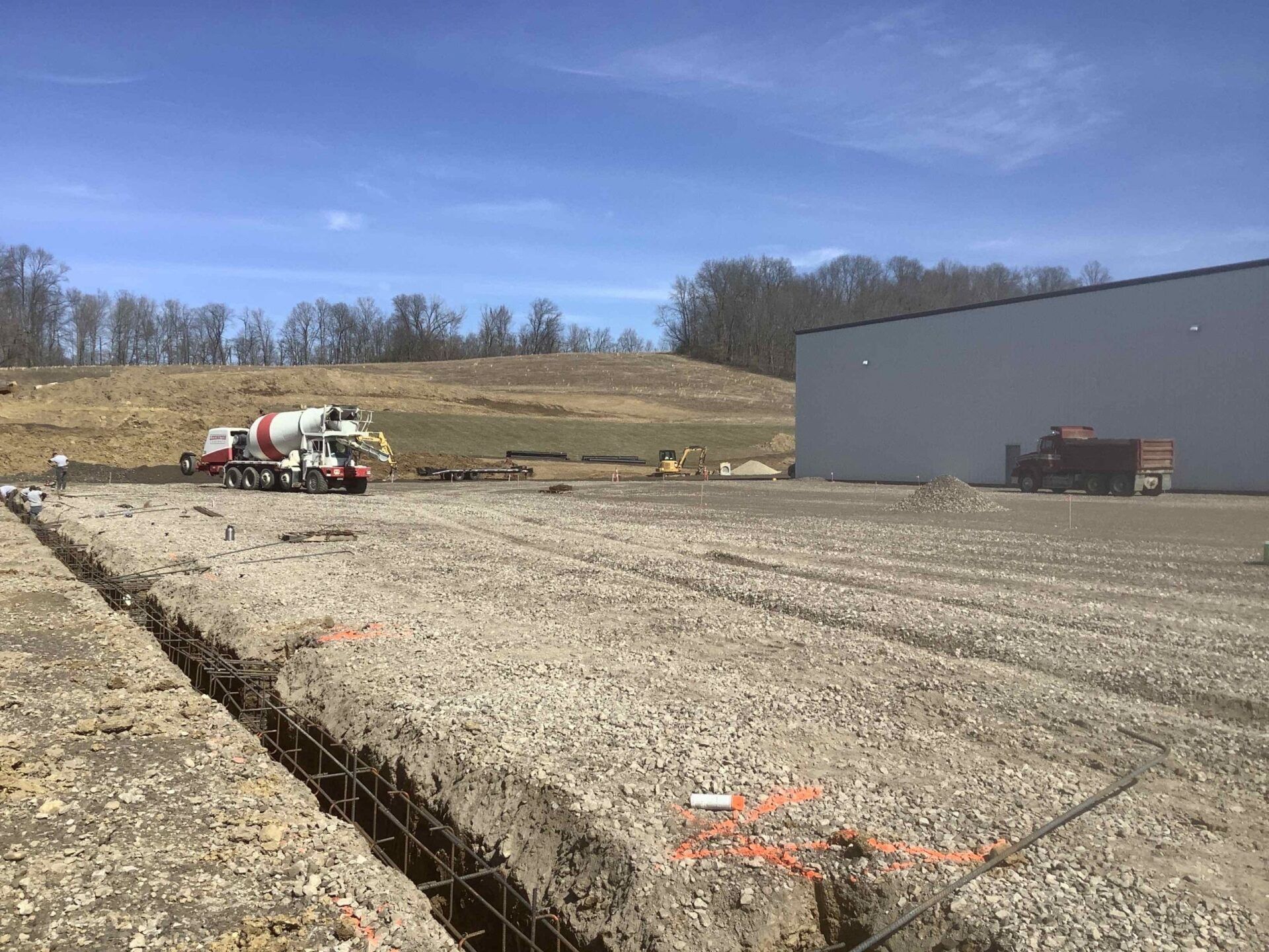 Construction site with a concrete mixer truck, trenches, and a building on a sunny day.