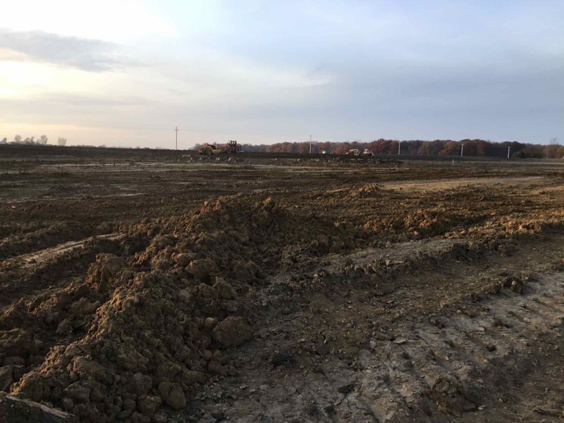 A large, plowed field with a cloudy sky in the background, near trees and a horizon.