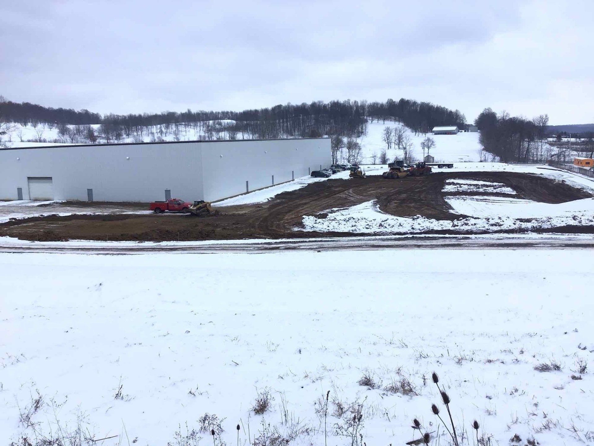 Snowy landscape with a large white building under construction; earthmoving equipment on a brown hillside.