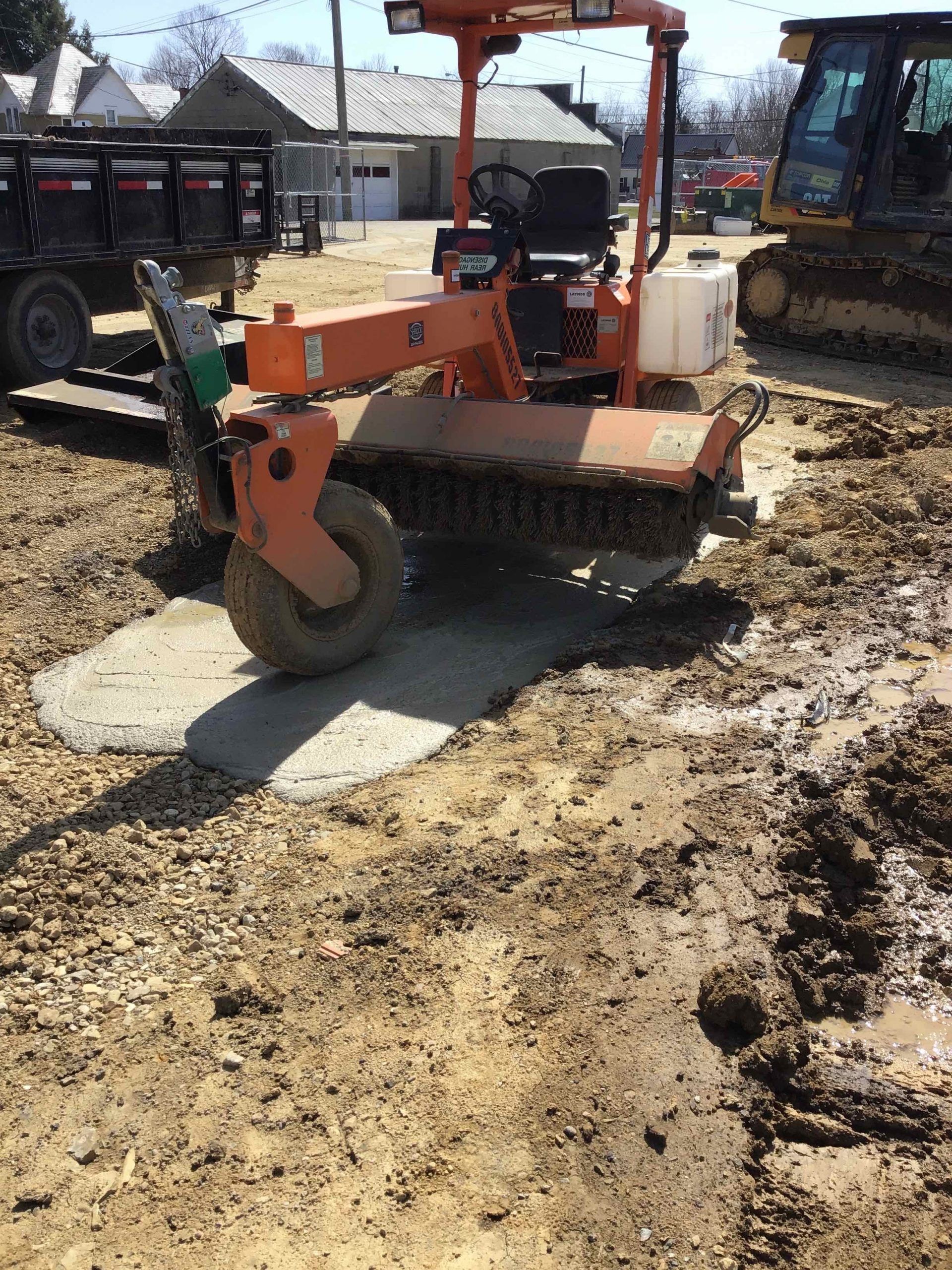 Orange machine sweeping mud on a construction site; truck and bulldozer visible.