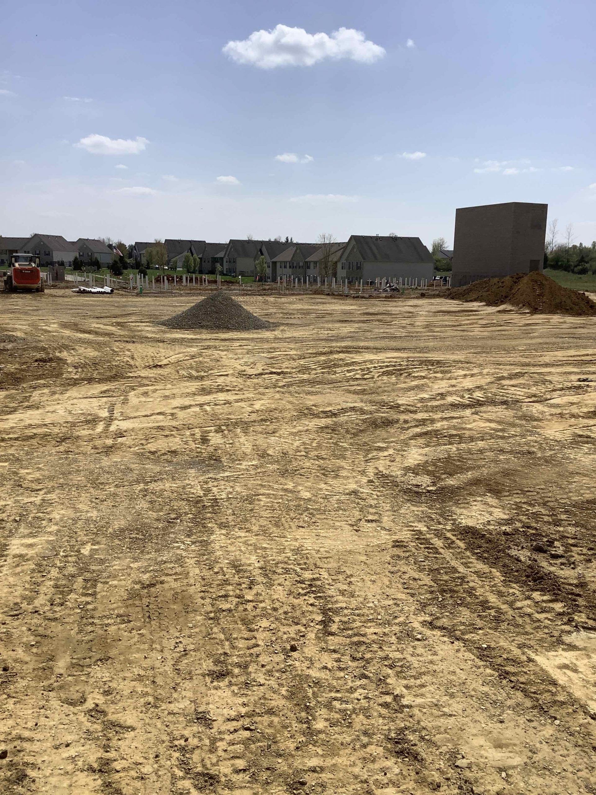 Construction site with cleared land, dirt, and partially built structures under a blue sky.