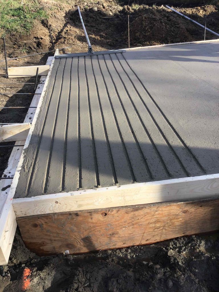 Newly poured concrete slab with evenly spaced control joints, surrounded by wood formwork.