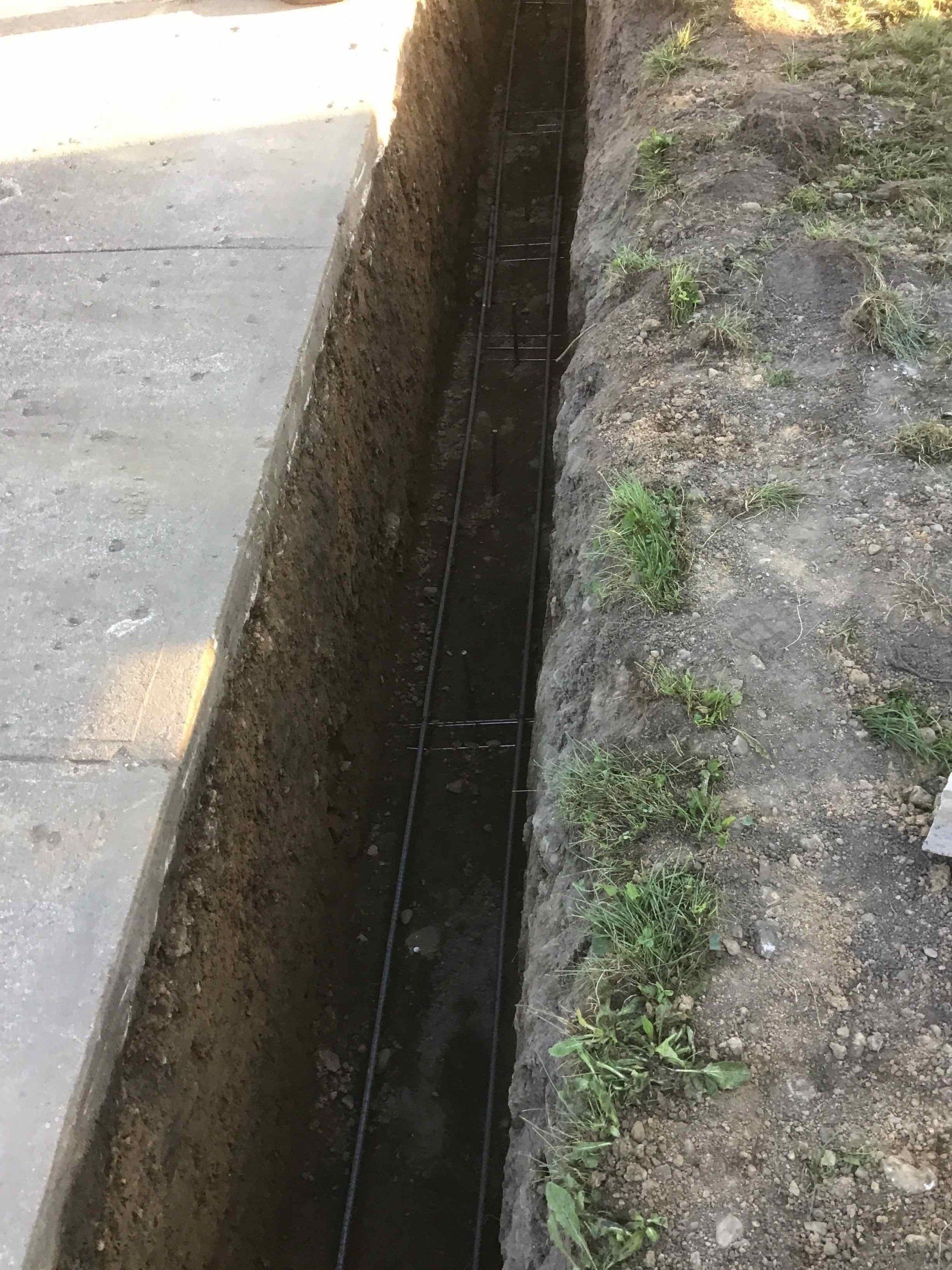 A long, narrow trench dug next to a concrete walkway, filled with water, and lined with string.