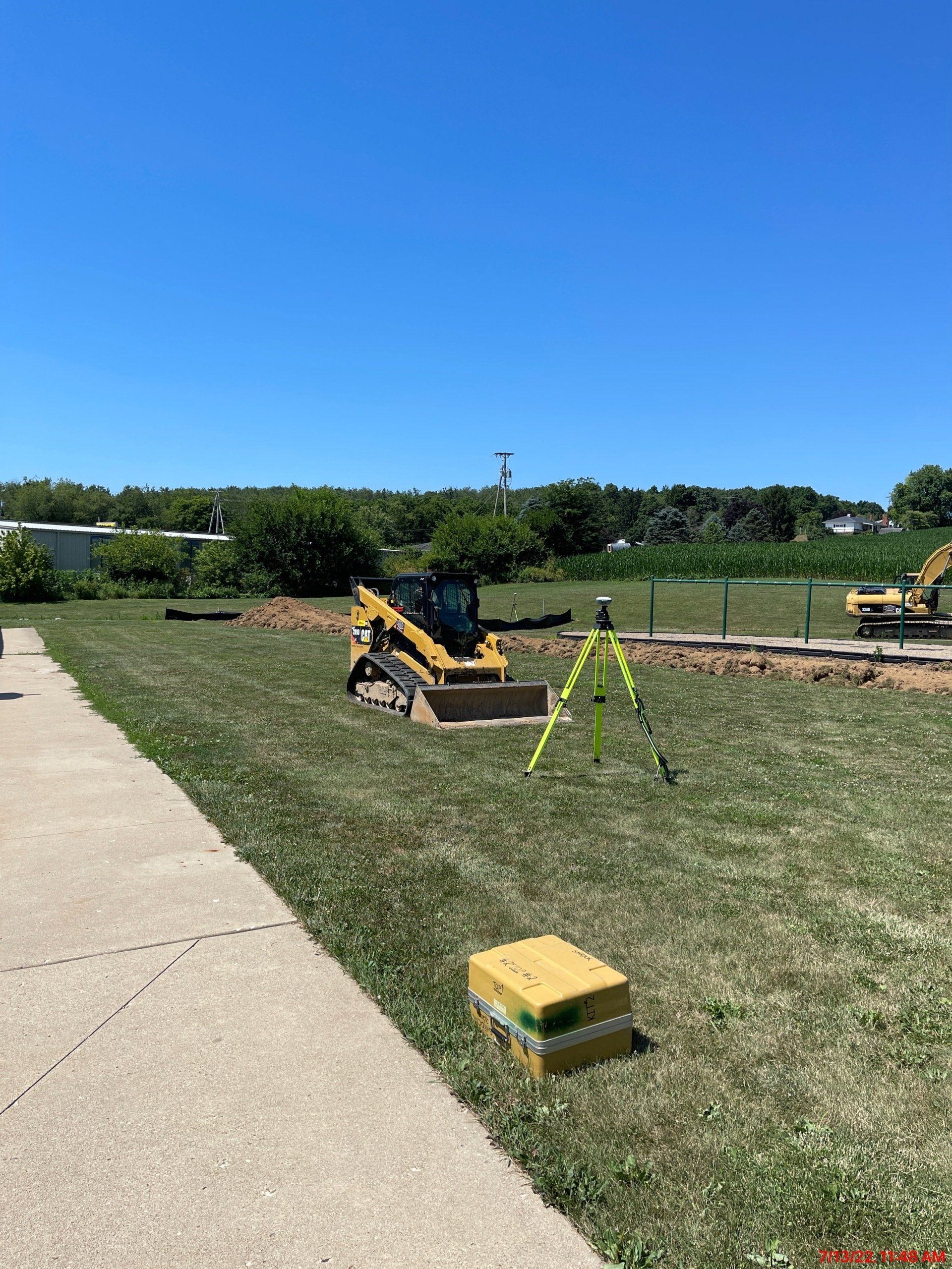 Construction site with yellow machinery and surveying equipment on green grass under a blue sky.