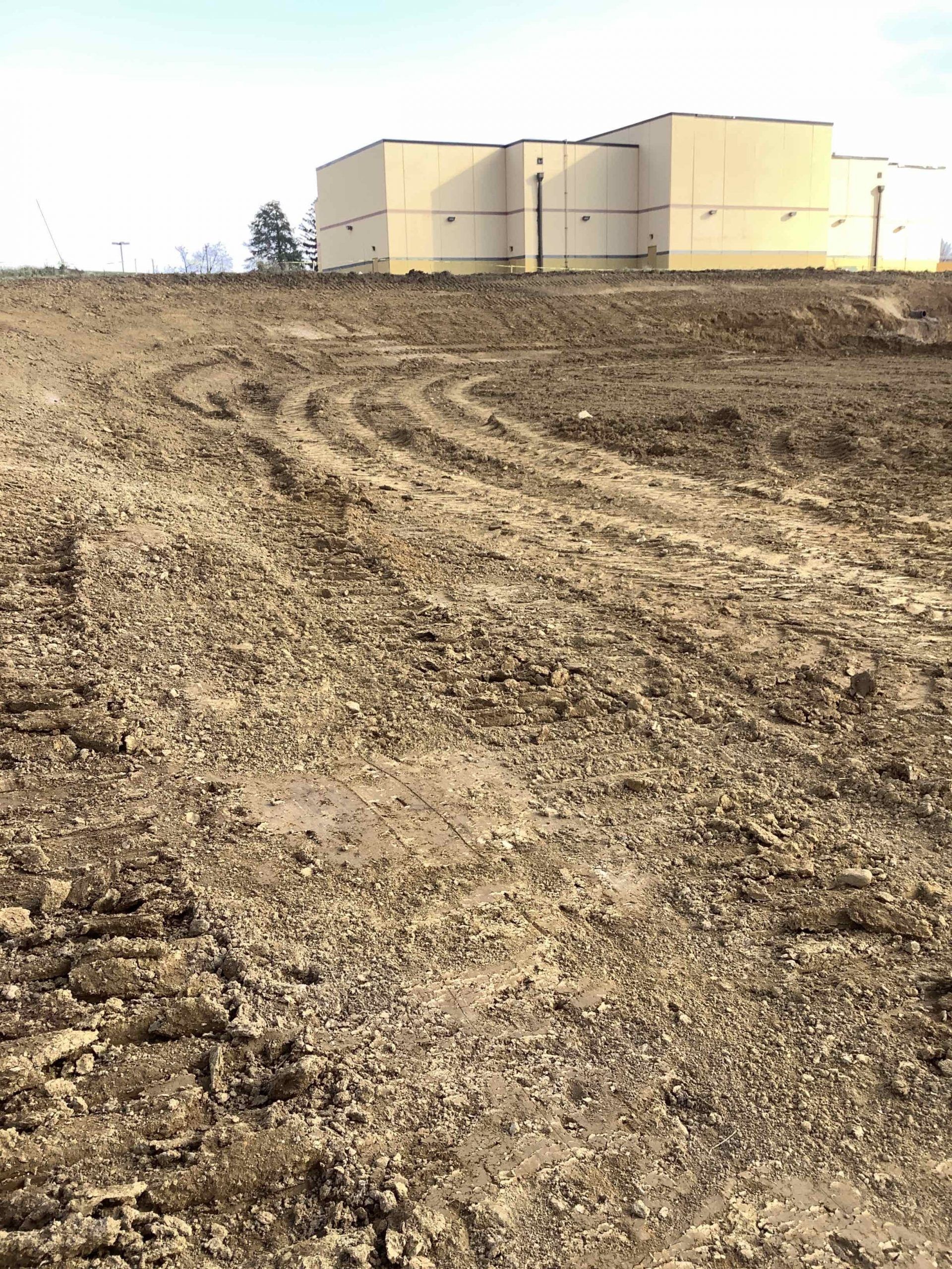 Muddy field with tire tracks in front of a tan building under a clear sky.