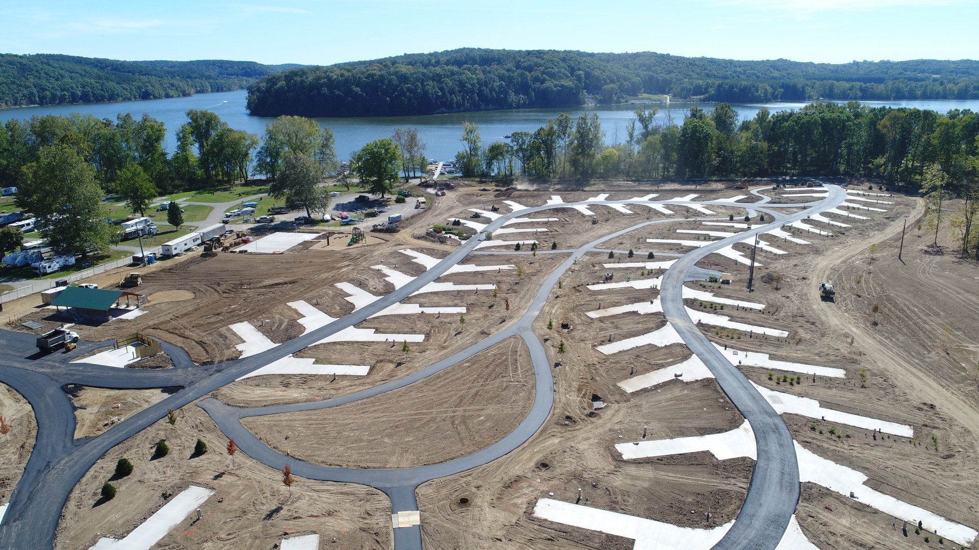 Aerial view of an RV park under construction near a lake with paved roads and campsites.