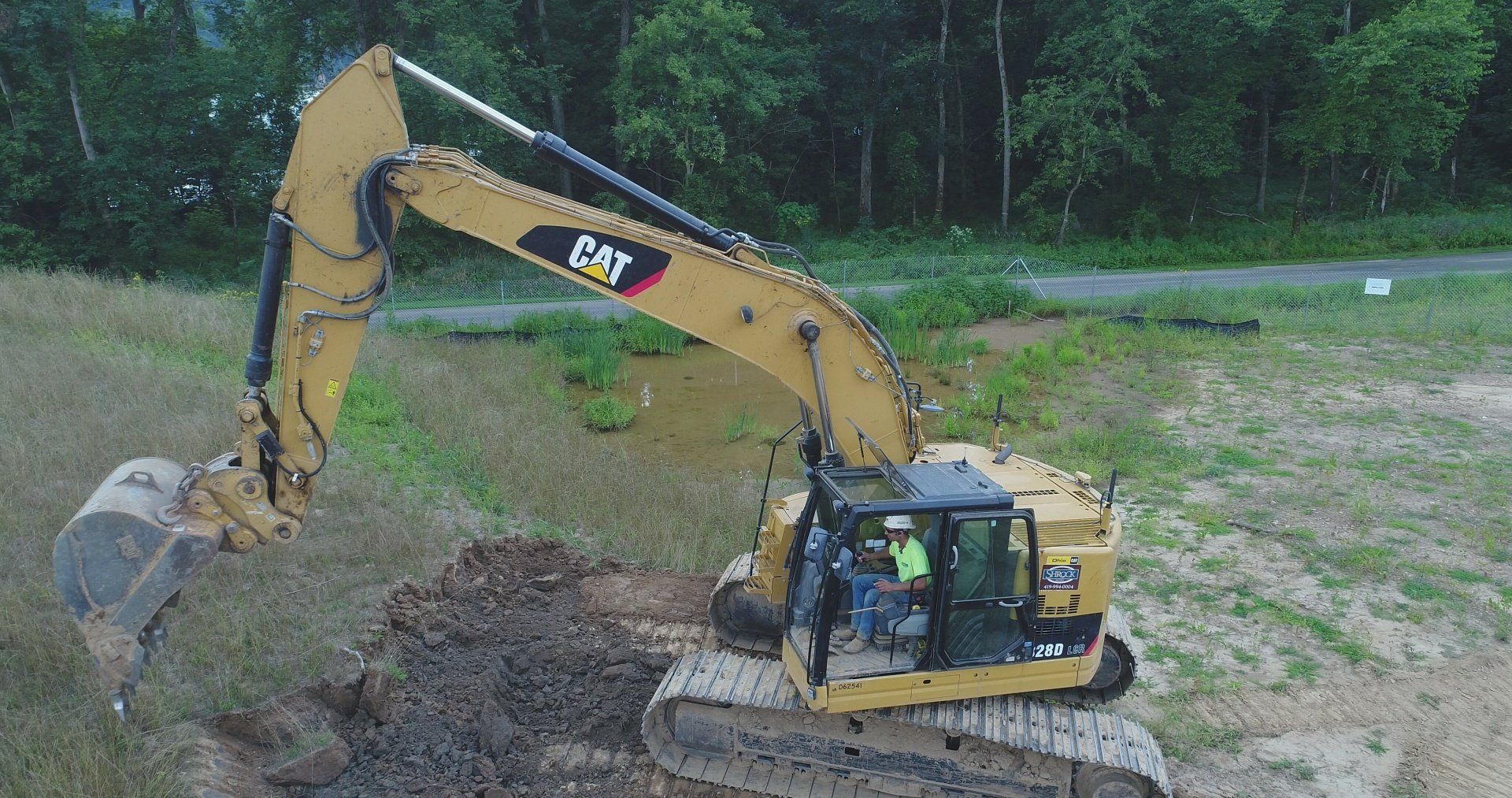 Yellow Caterpillar excavator digging earth near trees.