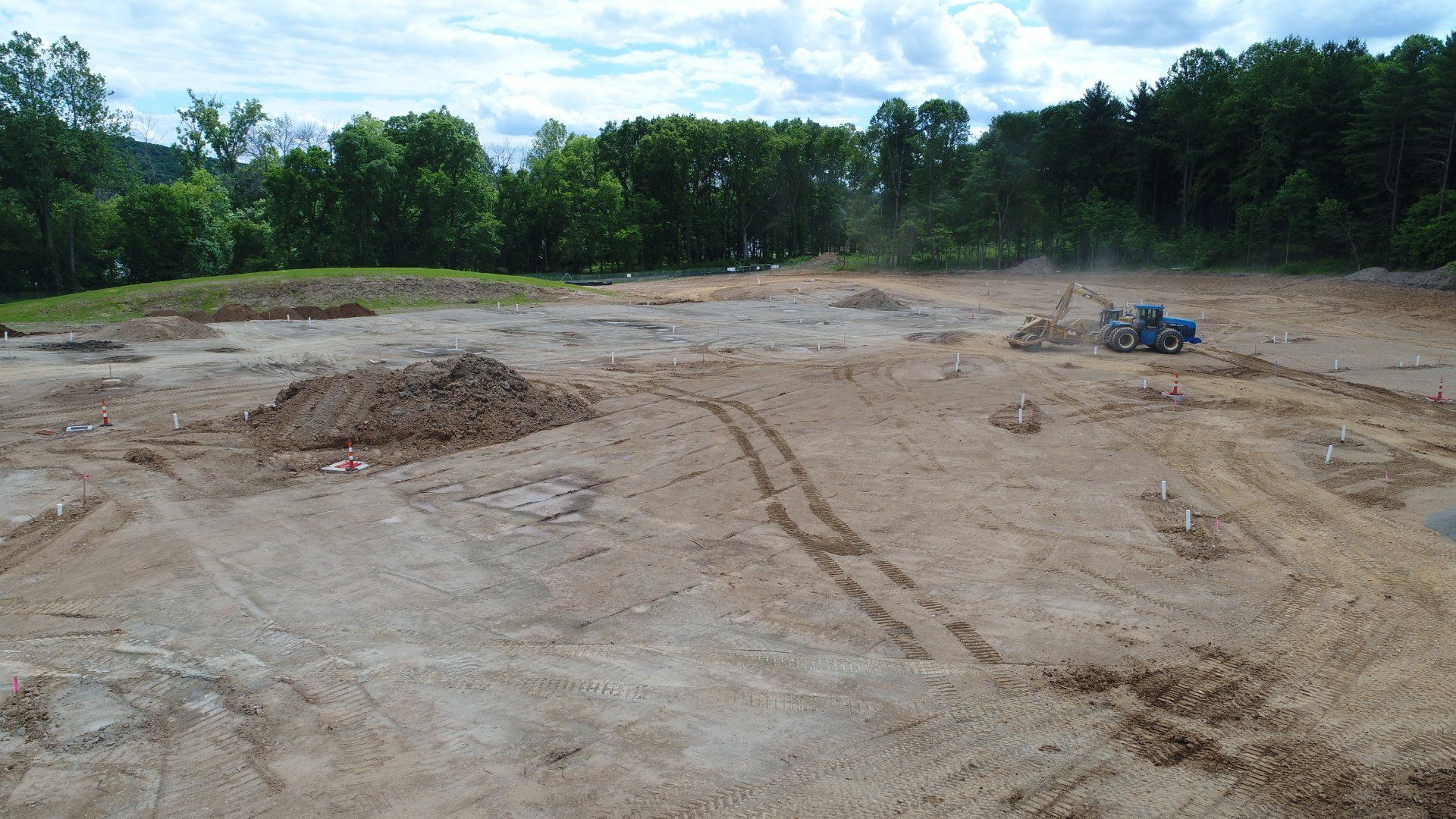 Construction site with exposed dirt and a blue bulldozer. Trees and a small hill in the background.