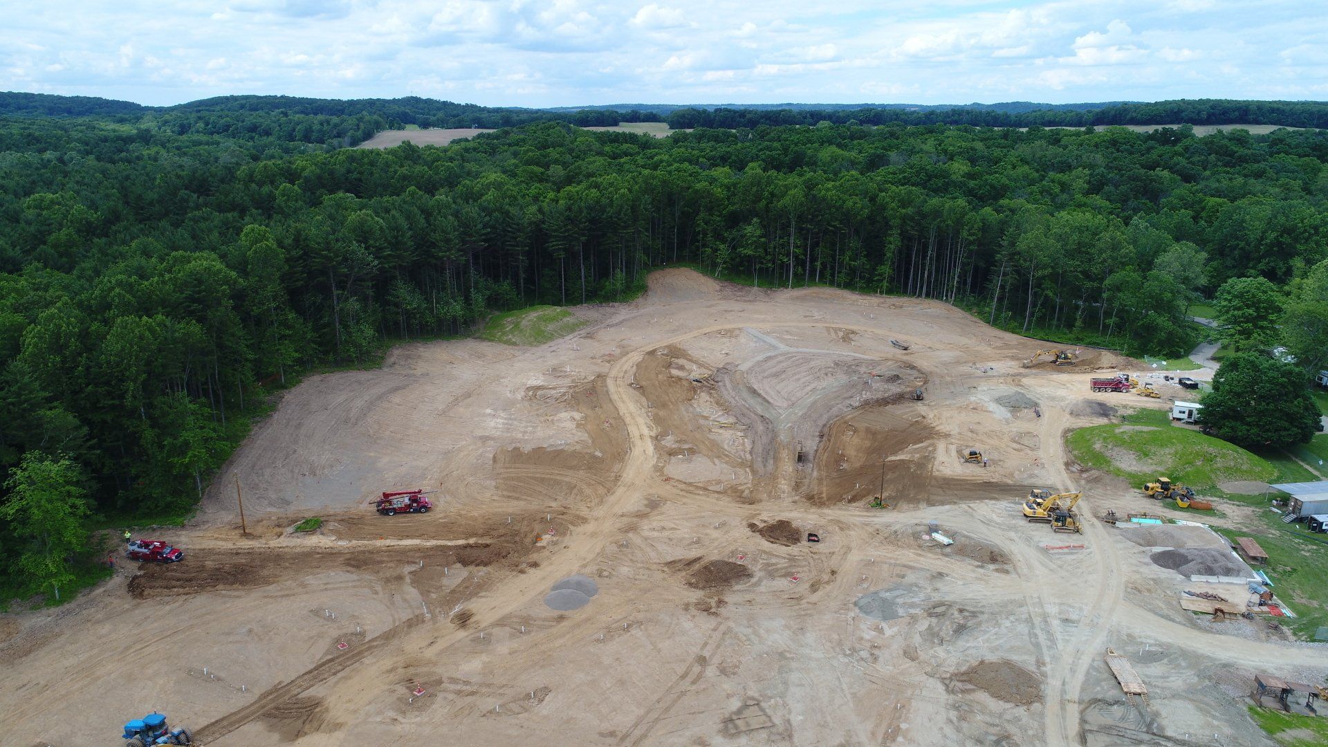 Aerial view of construction site with dirt, machinery, and bordering forest.