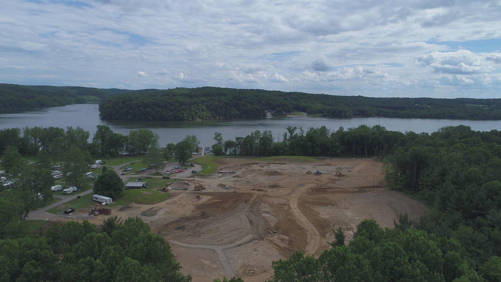 Aerial view of a clearing near a body of water, possibly for construction, with trees and cloudy sky.