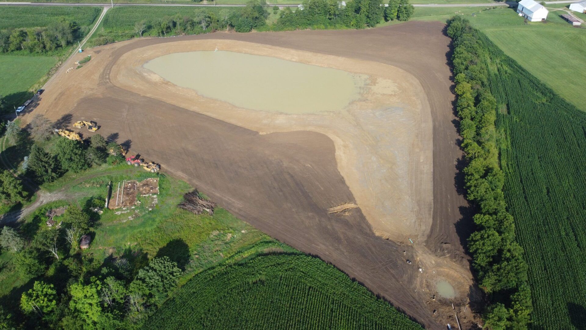 Aerial view of a newly constructed pond surrounded by brown dirt and green vegetation.