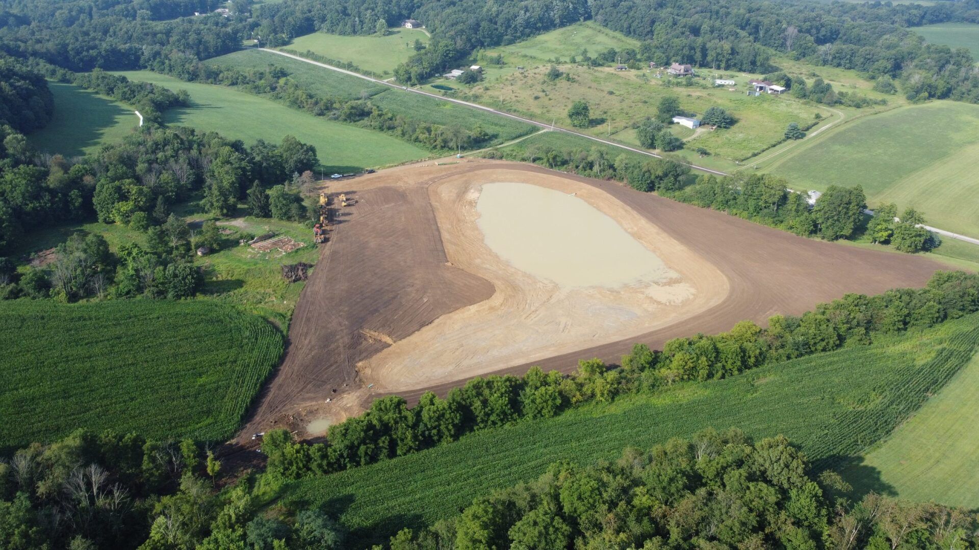 Aerial view of a cleared area in a rural landscape, with fields, trees, and earthwork in various shades of brown.