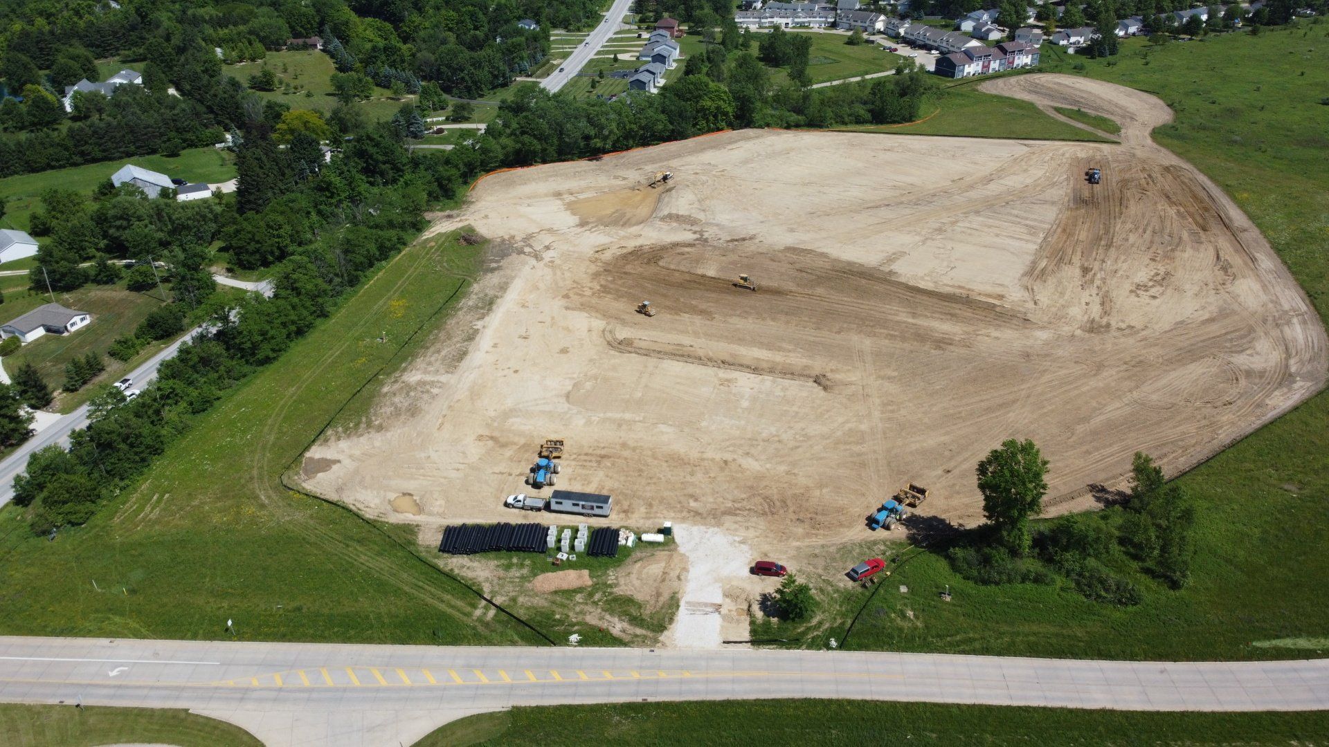 Aerial view of construction site clearing land; several vehicles and equipment on a dirt mound.