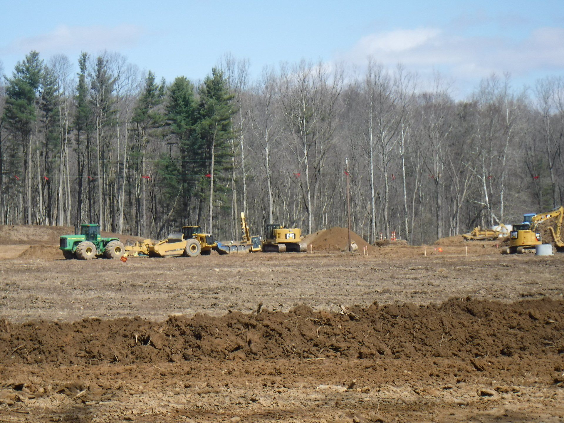 Construction site with heavy machinery, clearing land near a forest under a blue sky.